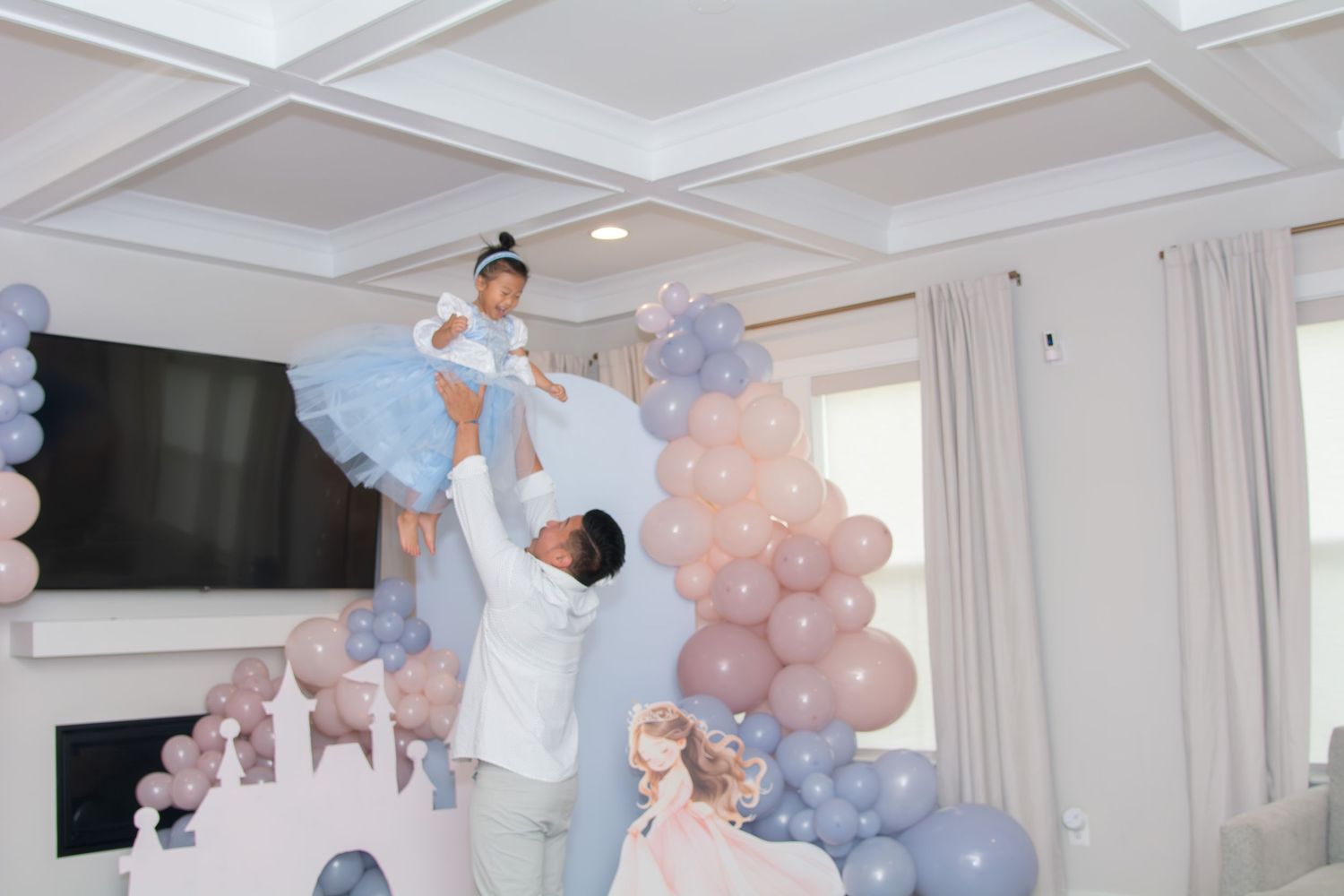 A celebratory scene with blue and pink balloon decorations in a bright modern living room with white coffered ceiling.