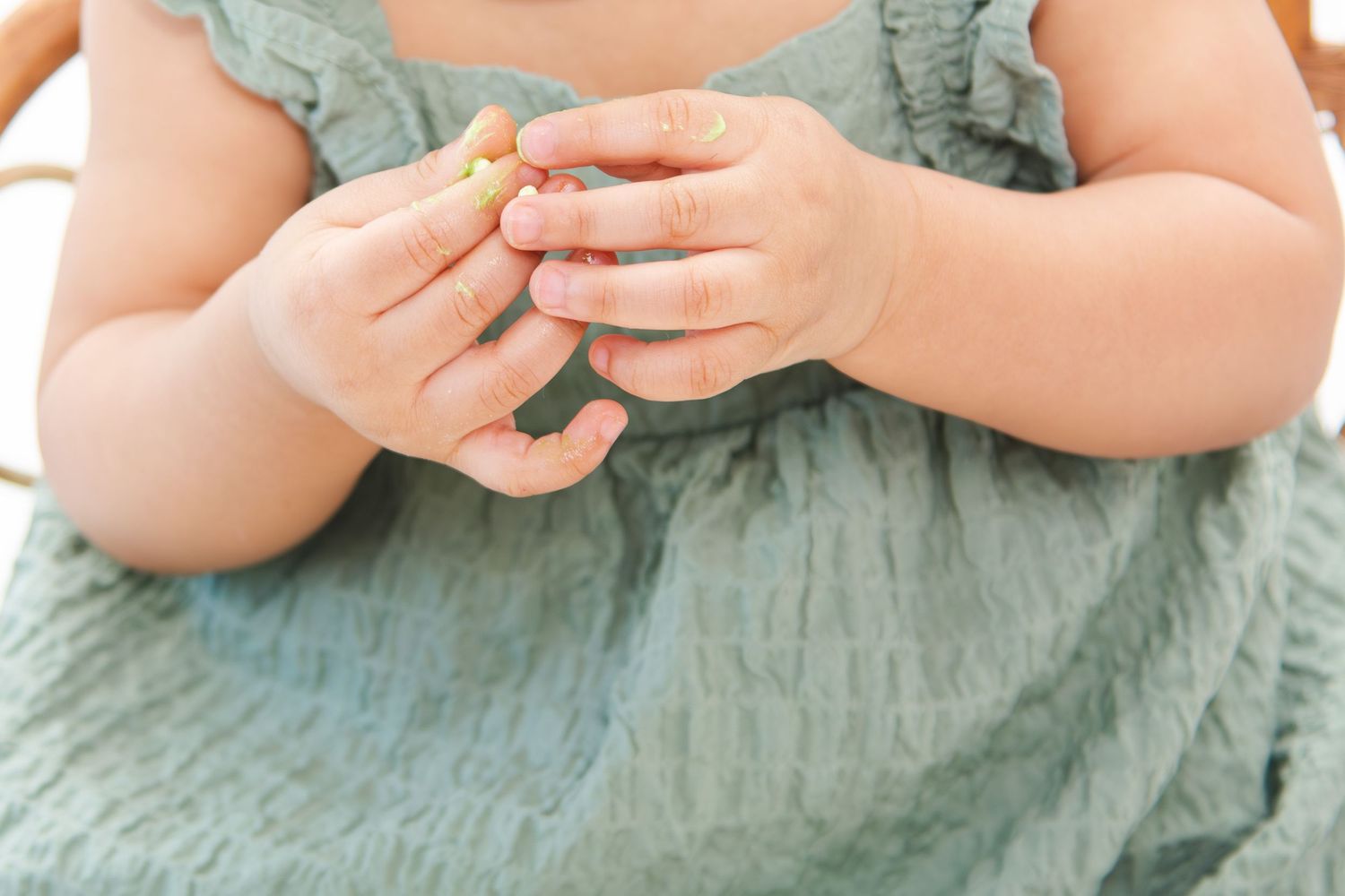Close-up of baby wearing sage green dress during professional photo session.