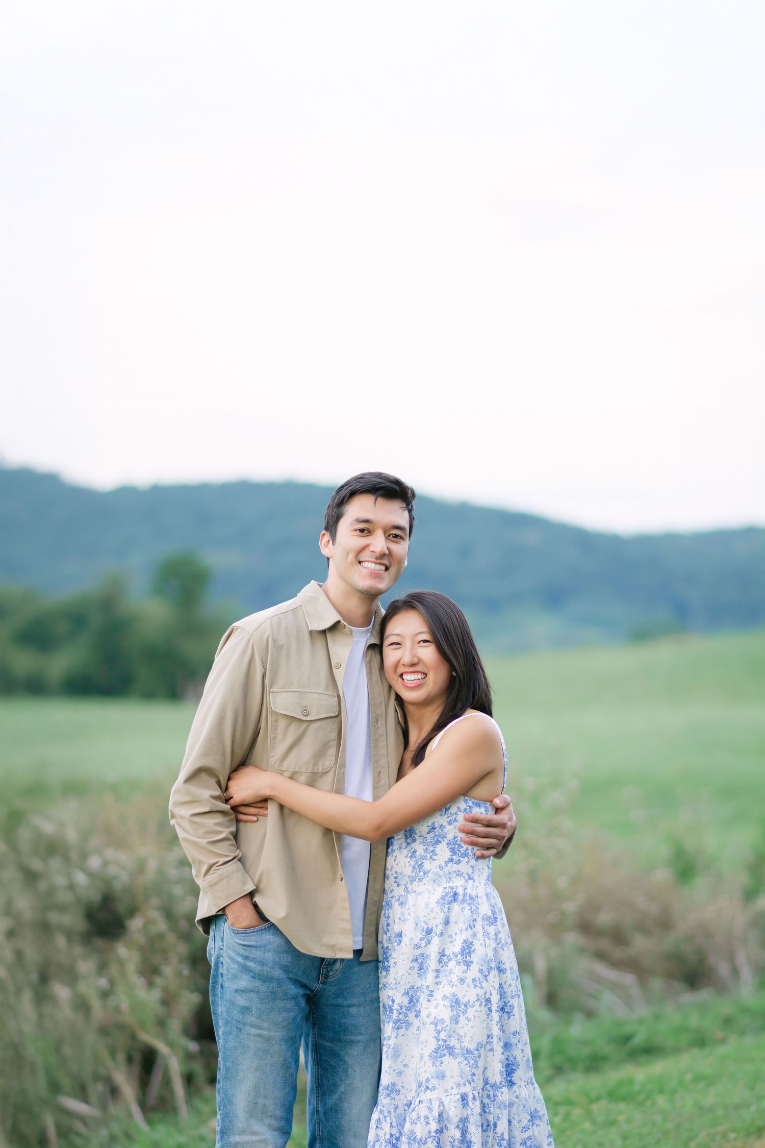 Couple in casual attire sharing an intimate moment against a scenic rural backdrop.