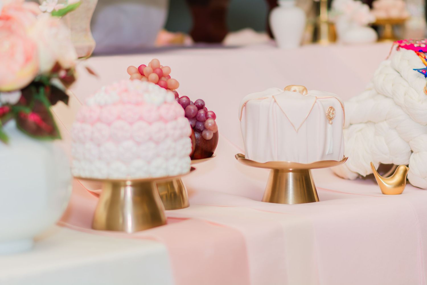 White cakes on gold pedestals with pink floral and fruit decorations.