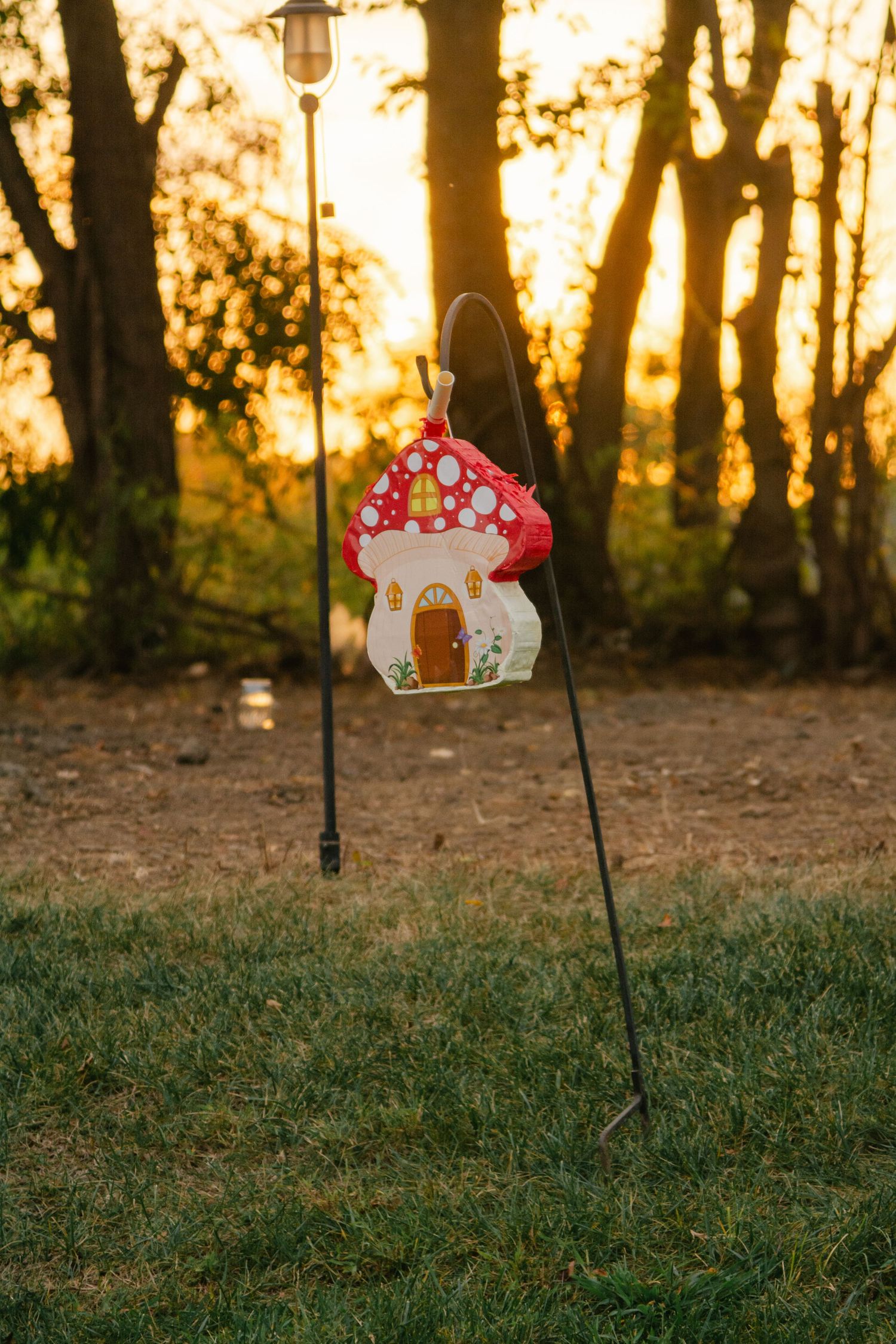 Decorative lanterns and ornaments hang against a golden sunset backdrop in a wooded area.