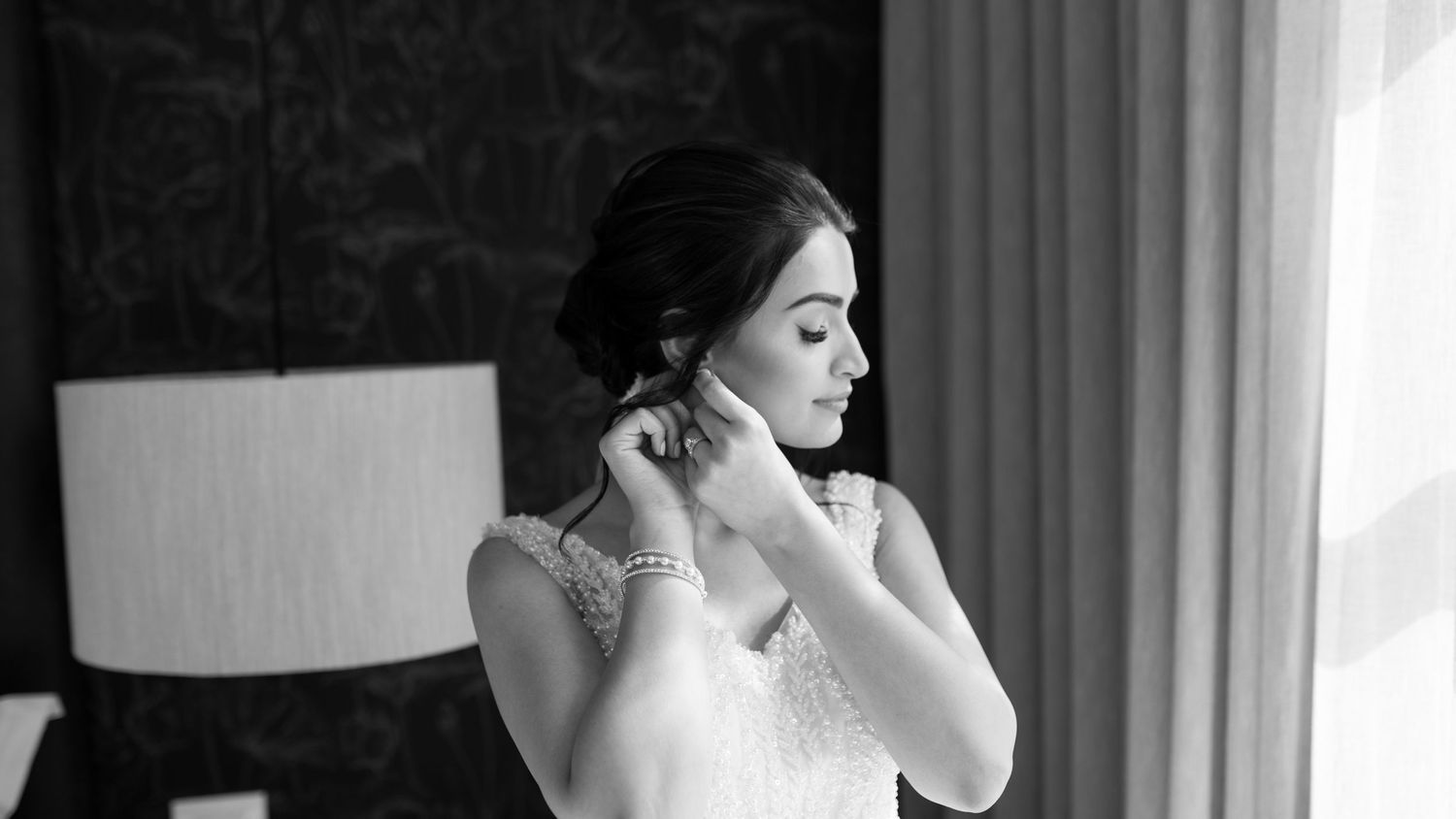 Elegant bridal preparation moment capturing jewelry details in window light.