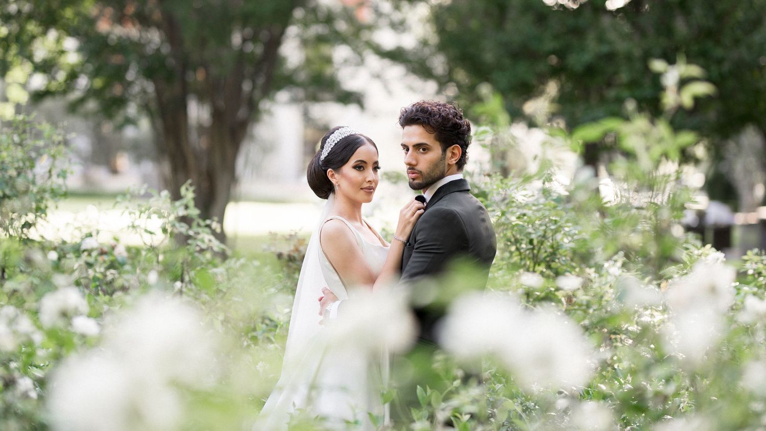 Newlyweds share a romantic moment in a garden setting surrounded by white flowers.
