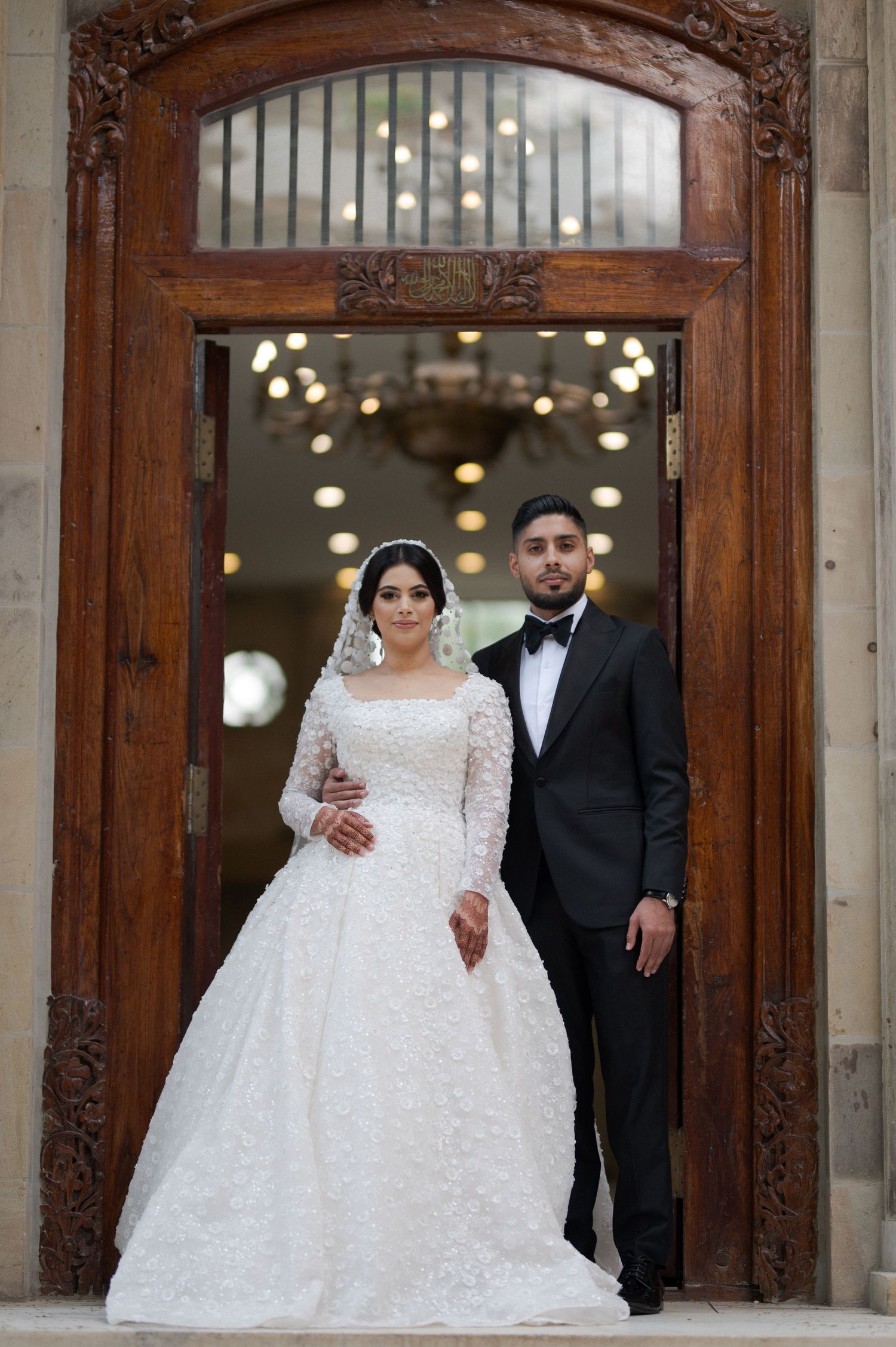 Wedding couple poses in ornate wooden doorway of elegant building.