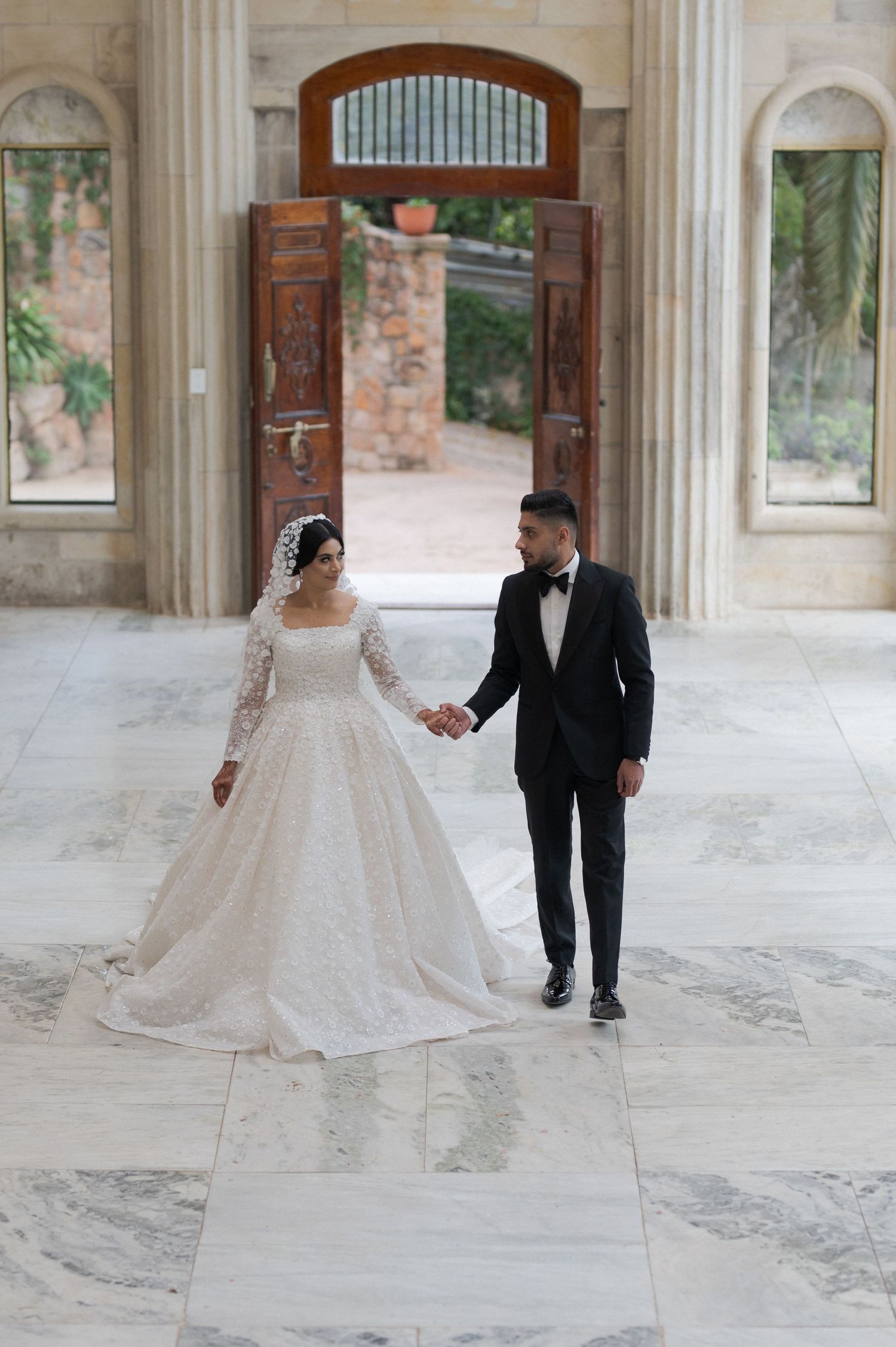 Bride and groom walking hand in hand through an elegant marble doorway.