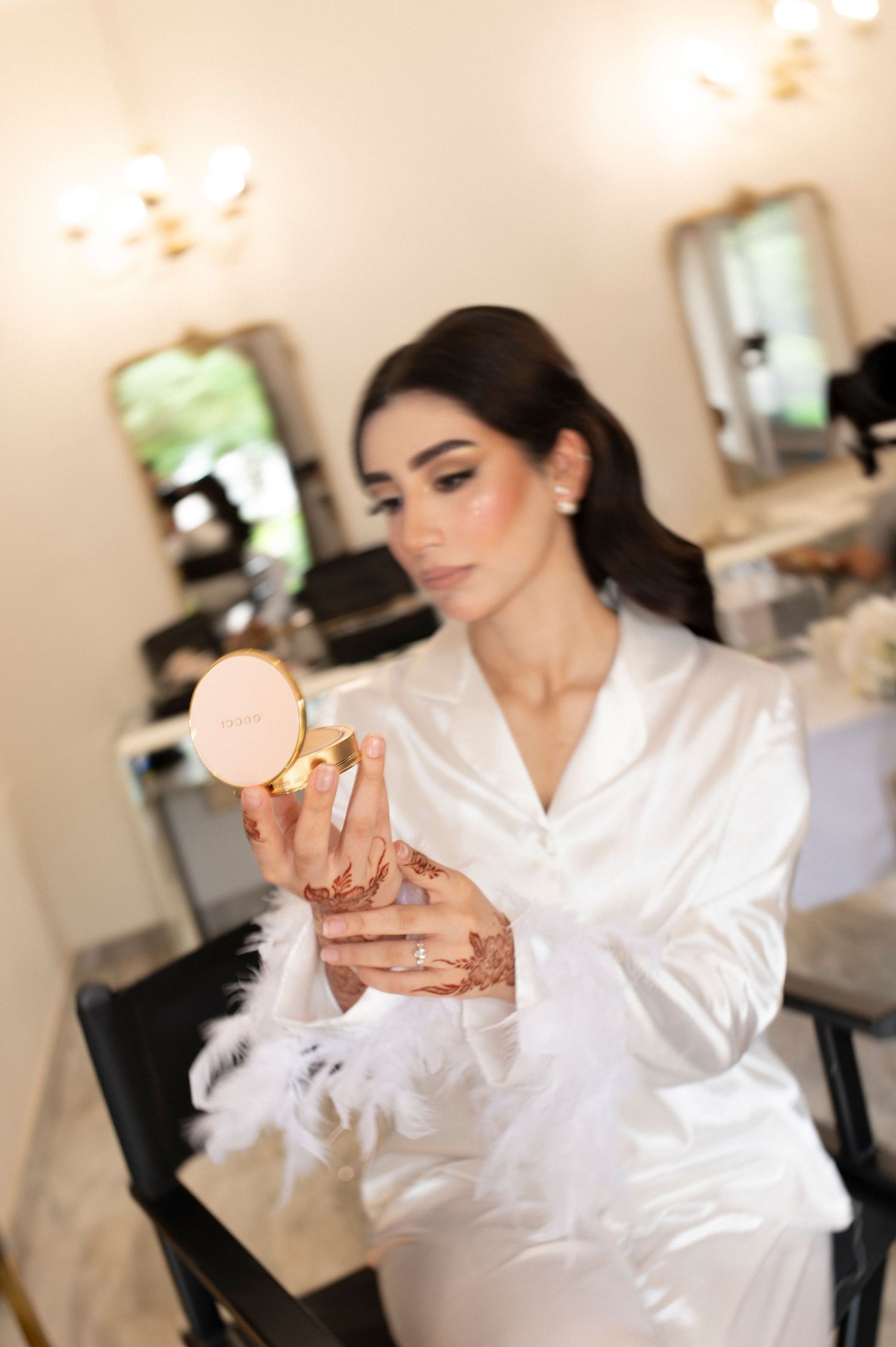A person in white satin robe applies makeup while getting ready for a special occasion.