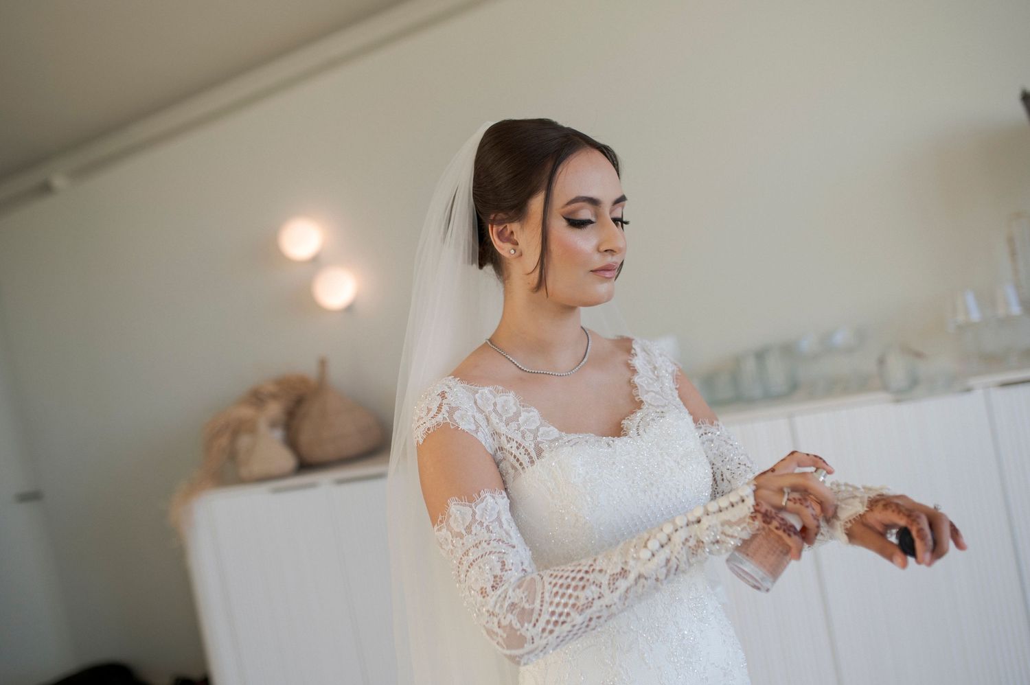 Close-up shot of bride in long-sleeve lace wedding dress adjusting jewelry.