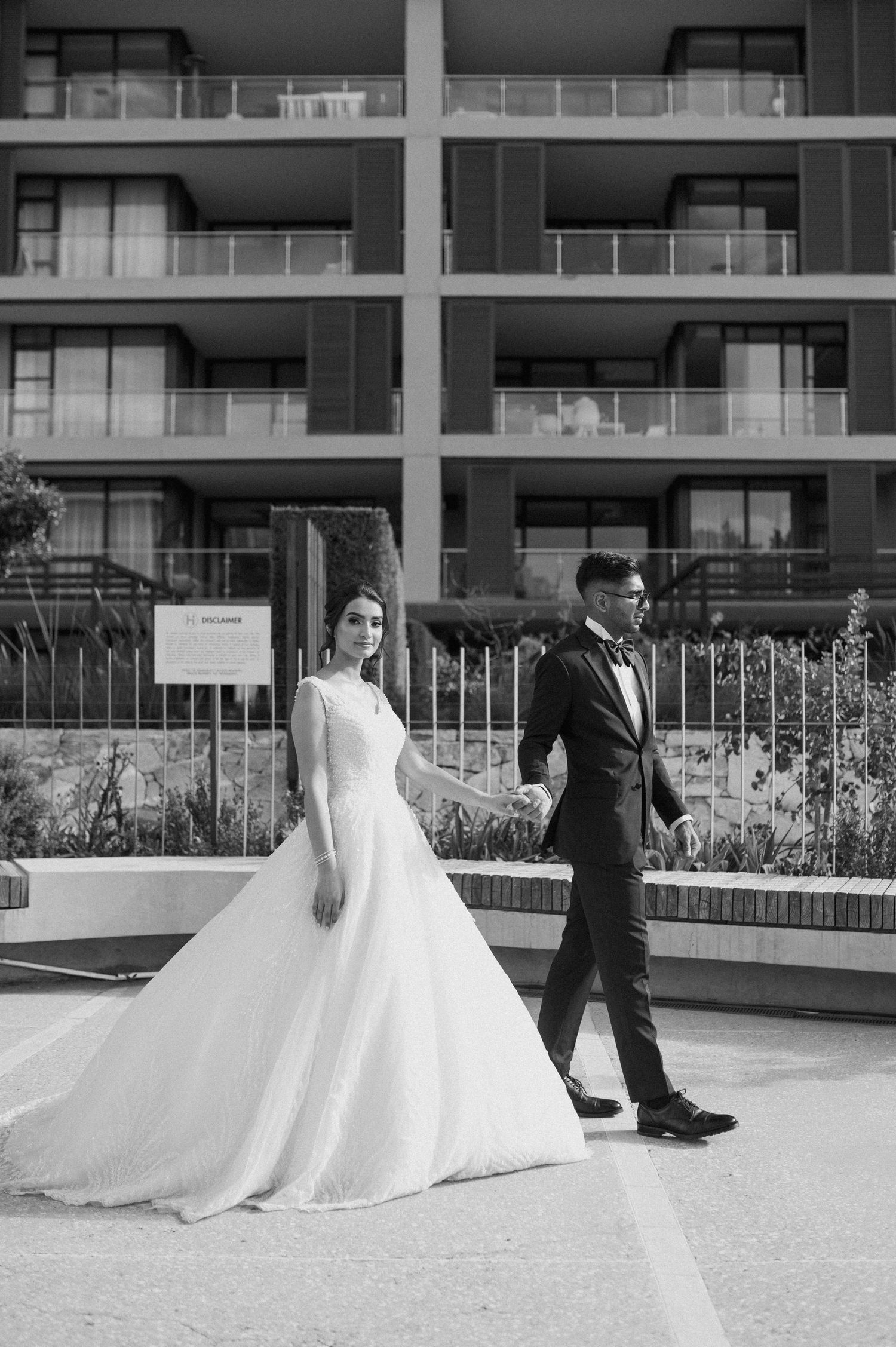 Artistic black and white shot of newlyweds walking near modern architecture.