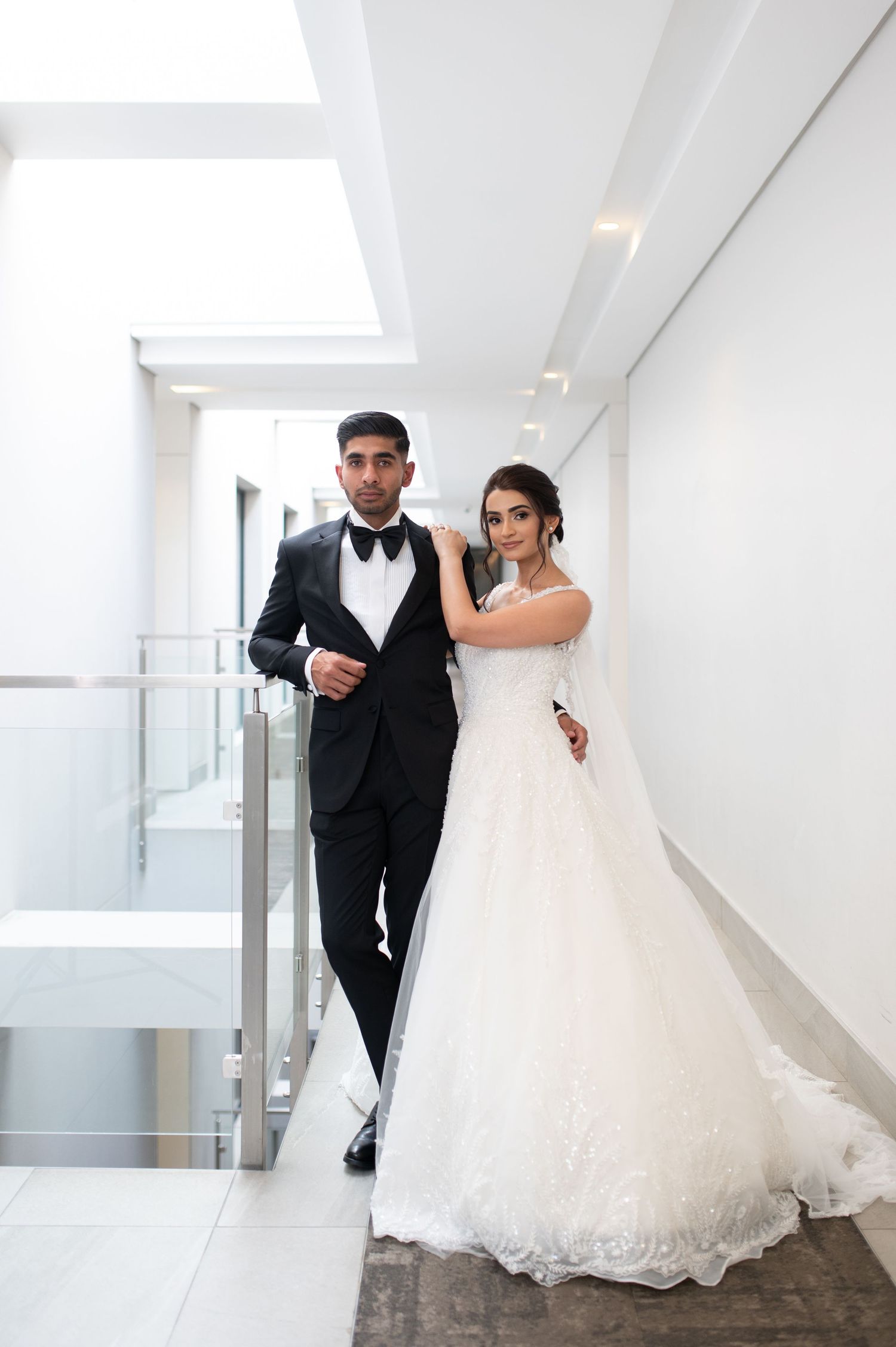 A couple poses in a modern white hallway on their wedding day, wearing traditional bridal attire.