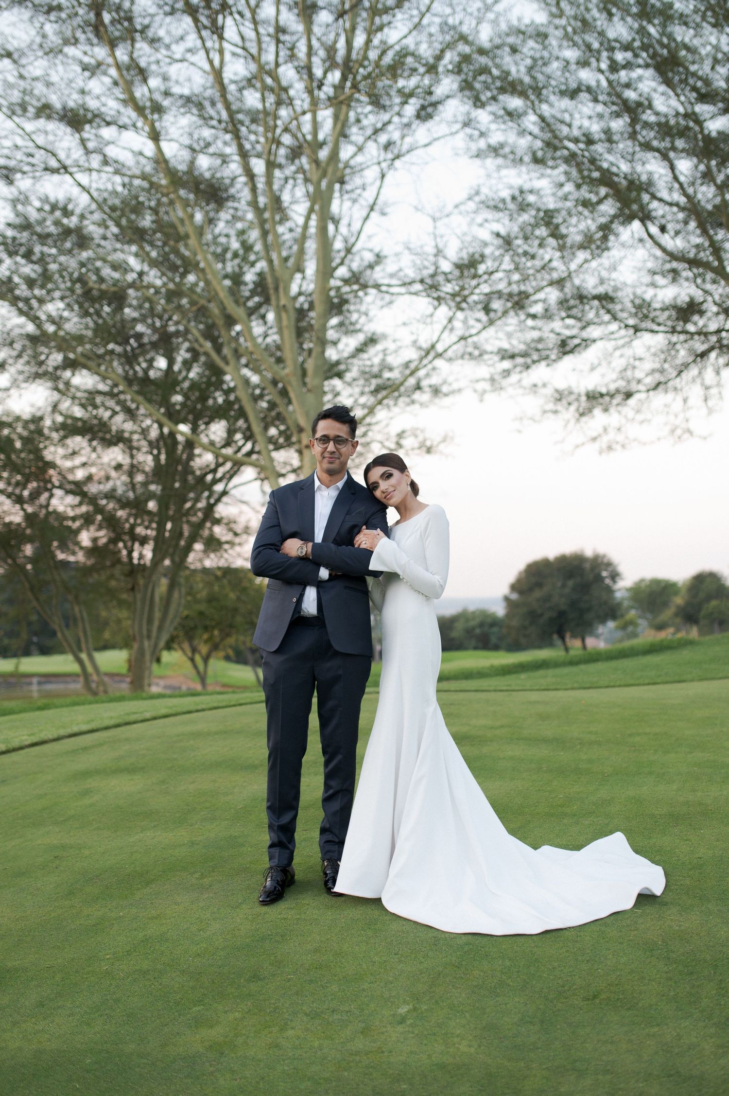 Stylish wedding couple poses together on golf course with bride in sleek white gown.