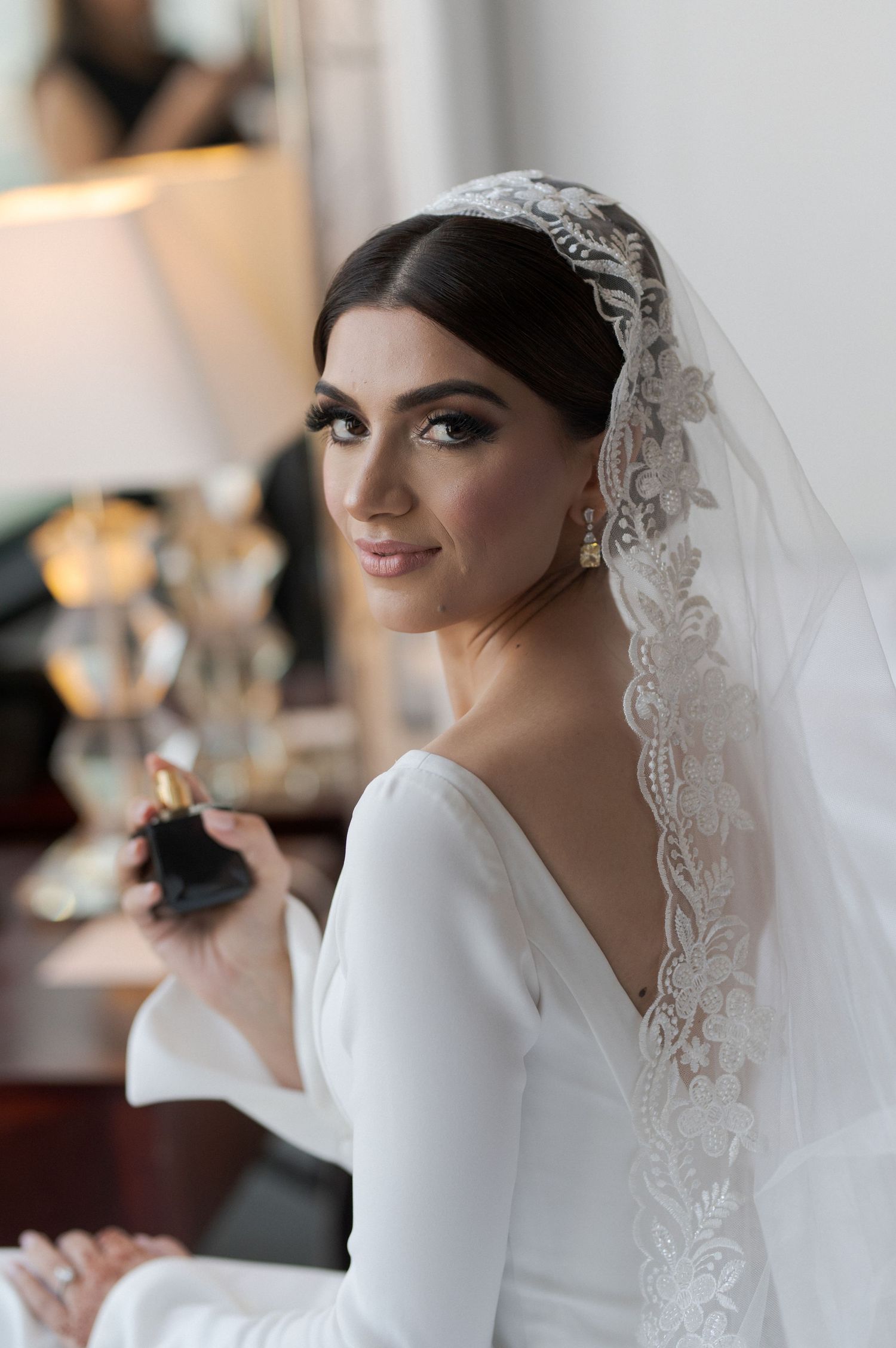 Elegant bride wearing white long-sleeved gown and lace veil with classic wedding day styling.