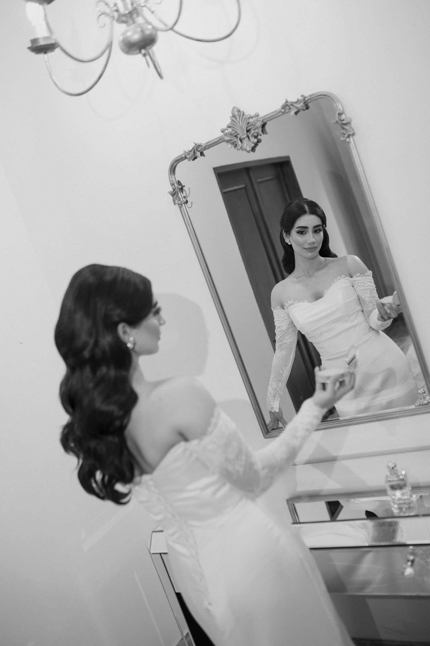 A reflection of a person in white dress looking into an ornate framed mirror.