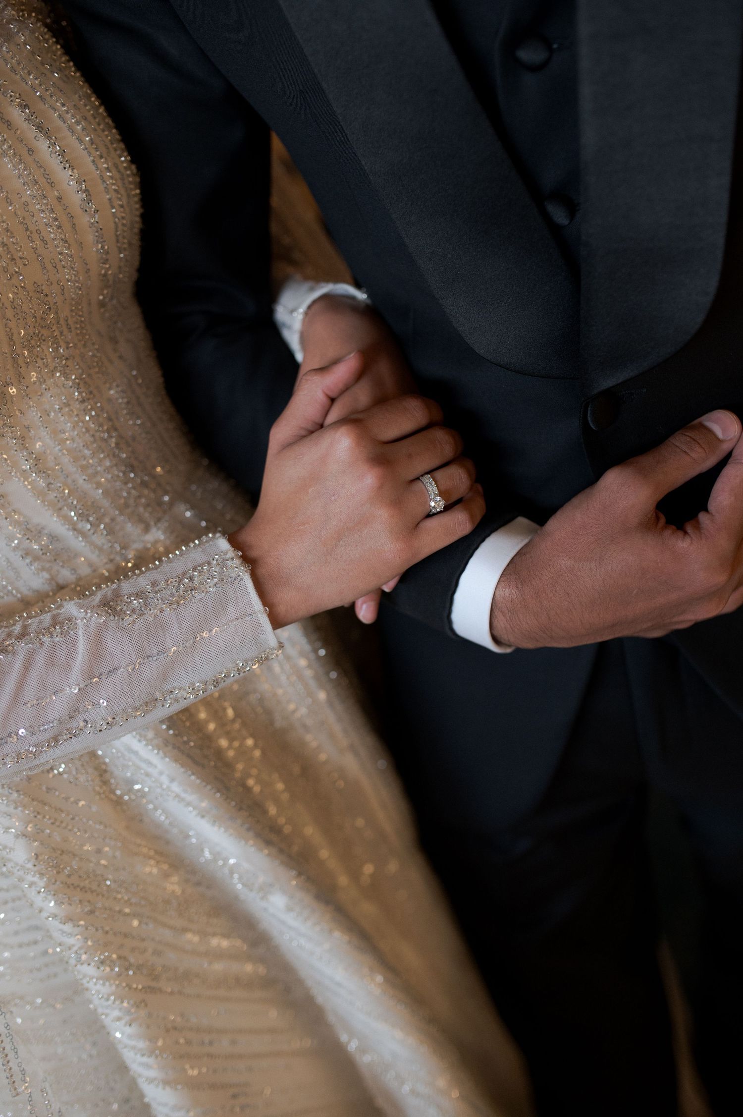 Detail shot of couple's hands with wedding ring visible against formal attire.