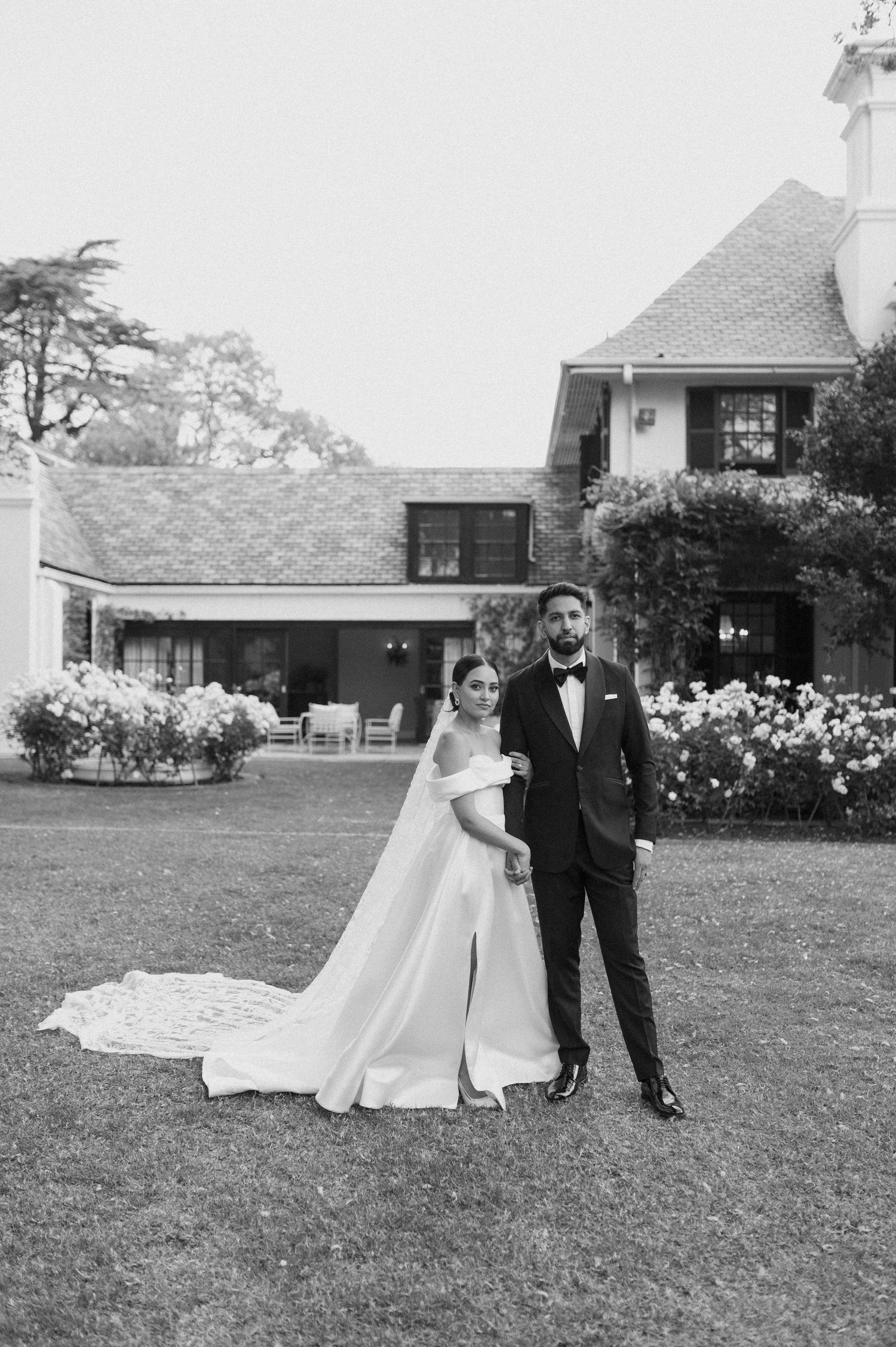 A classic black and white wedding portrait in front of a colonial-style mansion.