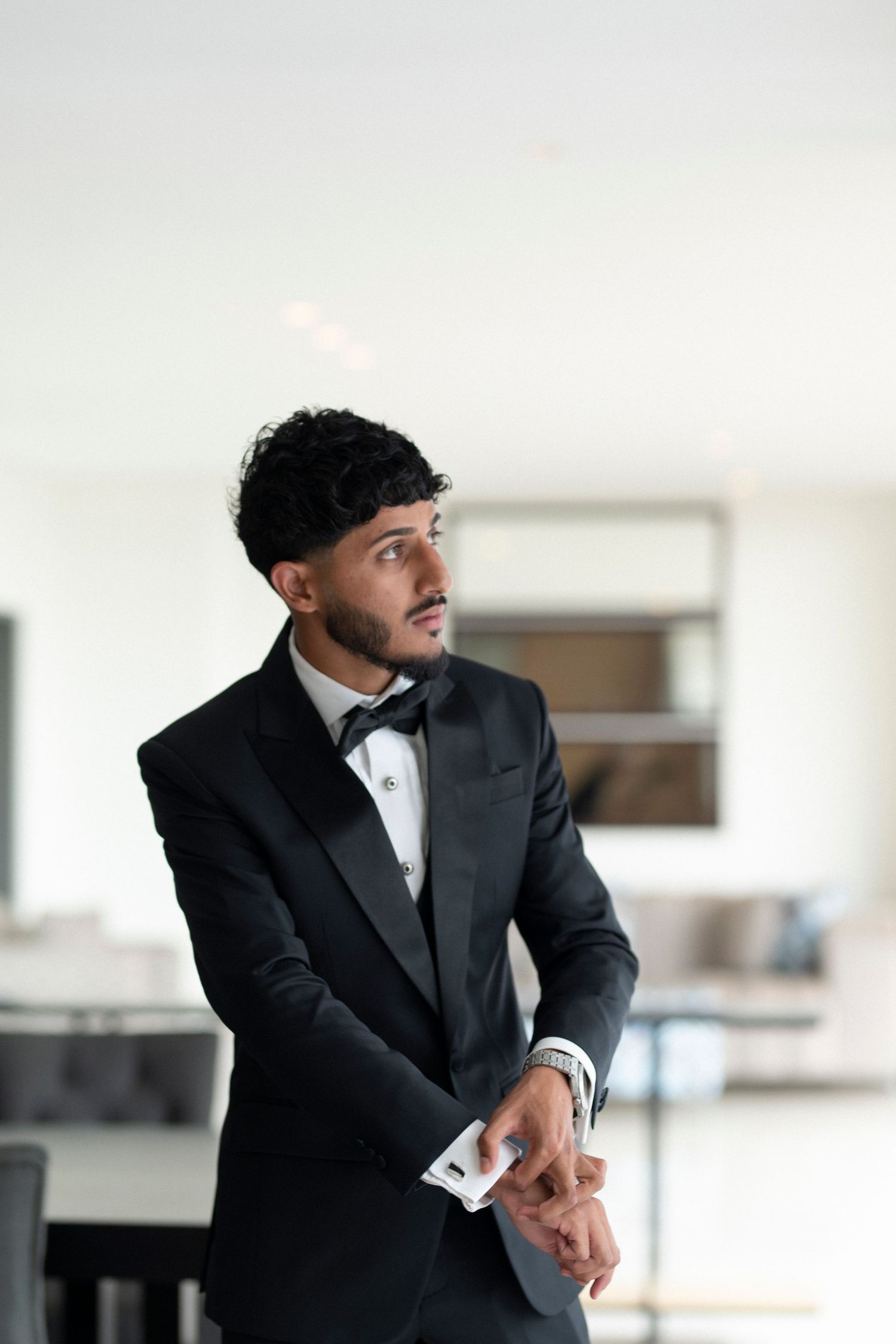 Groom in black tuxedo adjusting his cuffs.
