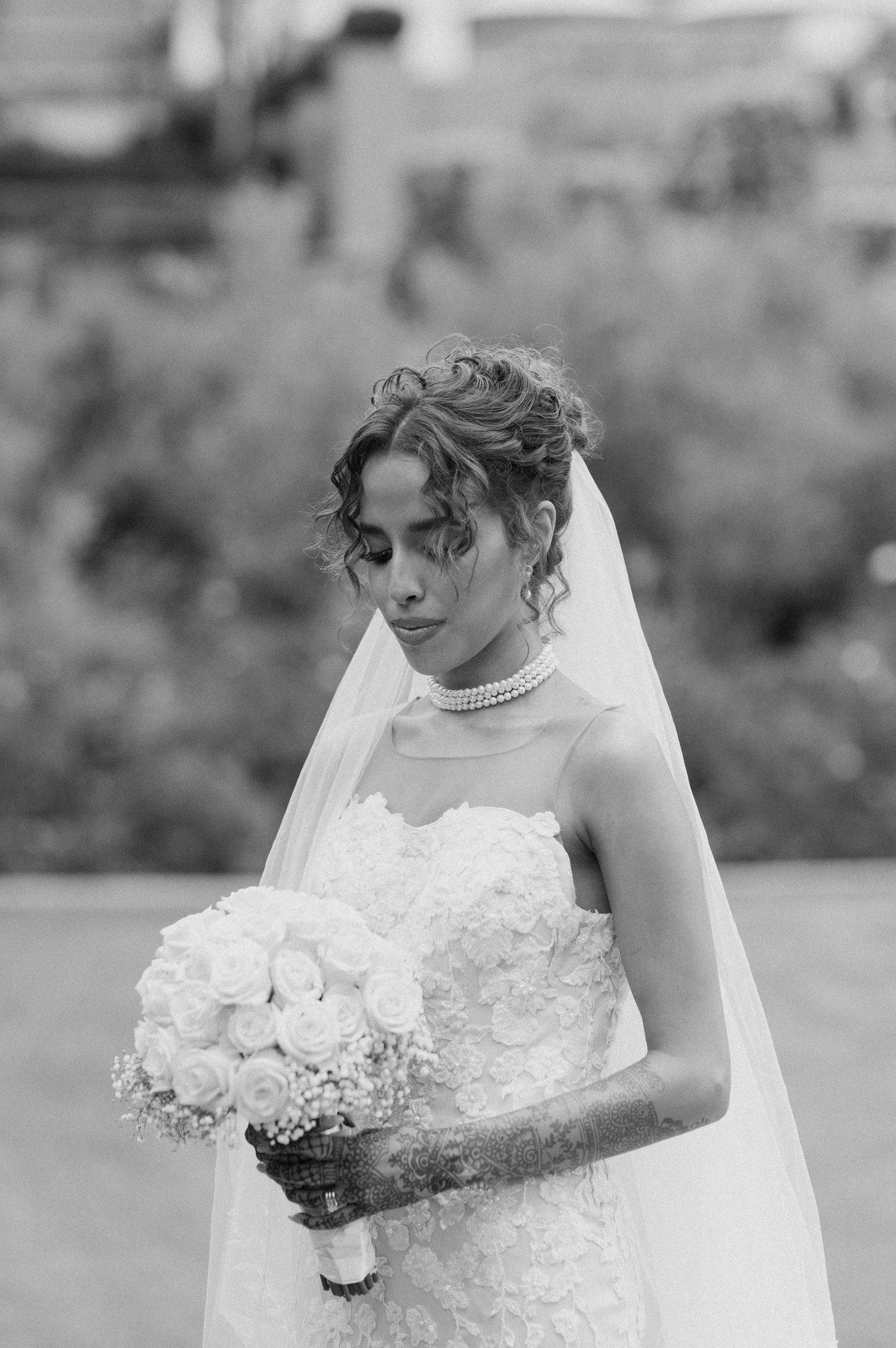 Black and white portrait of a bride holding a bouquet while wearing an elegant white lace gown and veil.