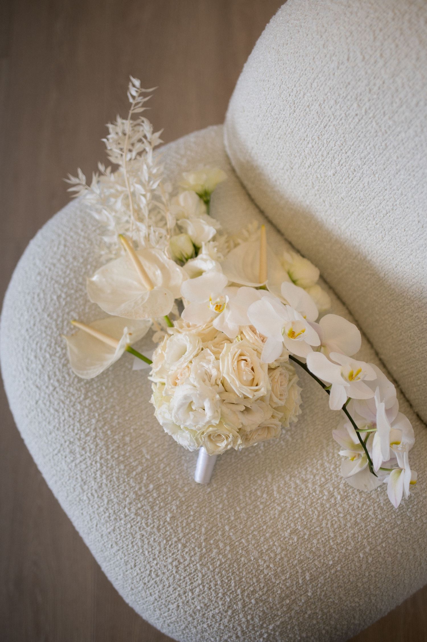 White bridal bouquet featuring roses, orchids and delicate floral arrangements on light colored surface.