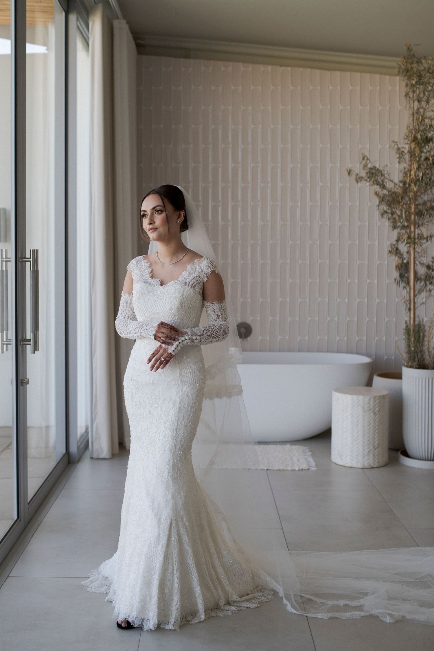 Full-length view of a lace wedding gown in a modern room with white bathtub.