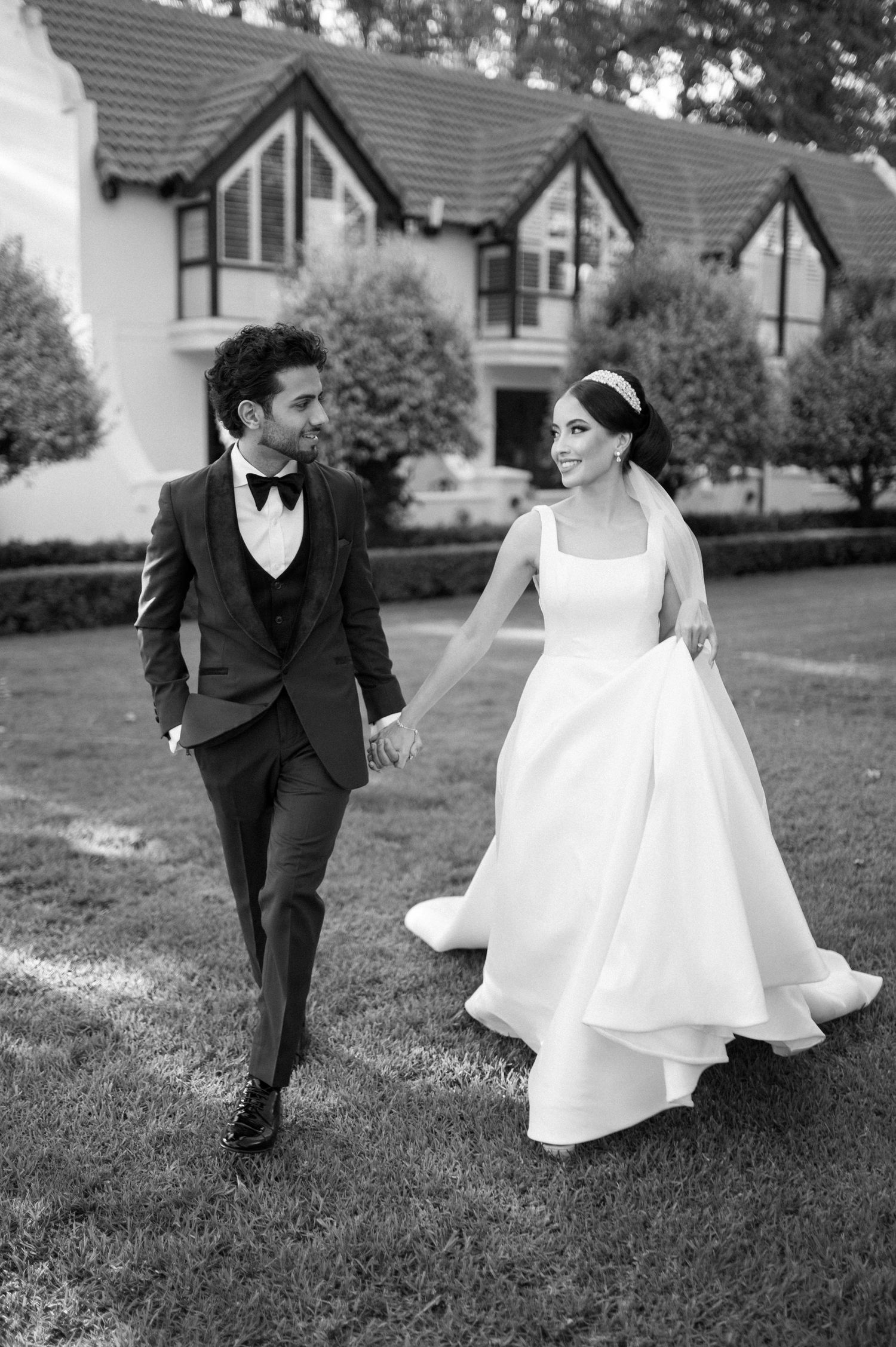 Black and white photo of couple walking joyfully on lawn during wedding celebration.