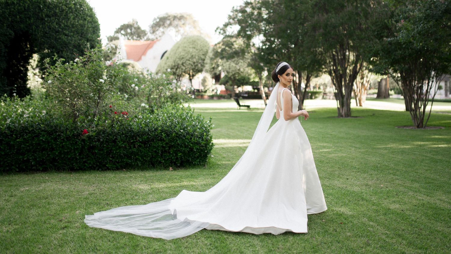 Elegant wedding dress with flowing train photographed in a lush garden setting.