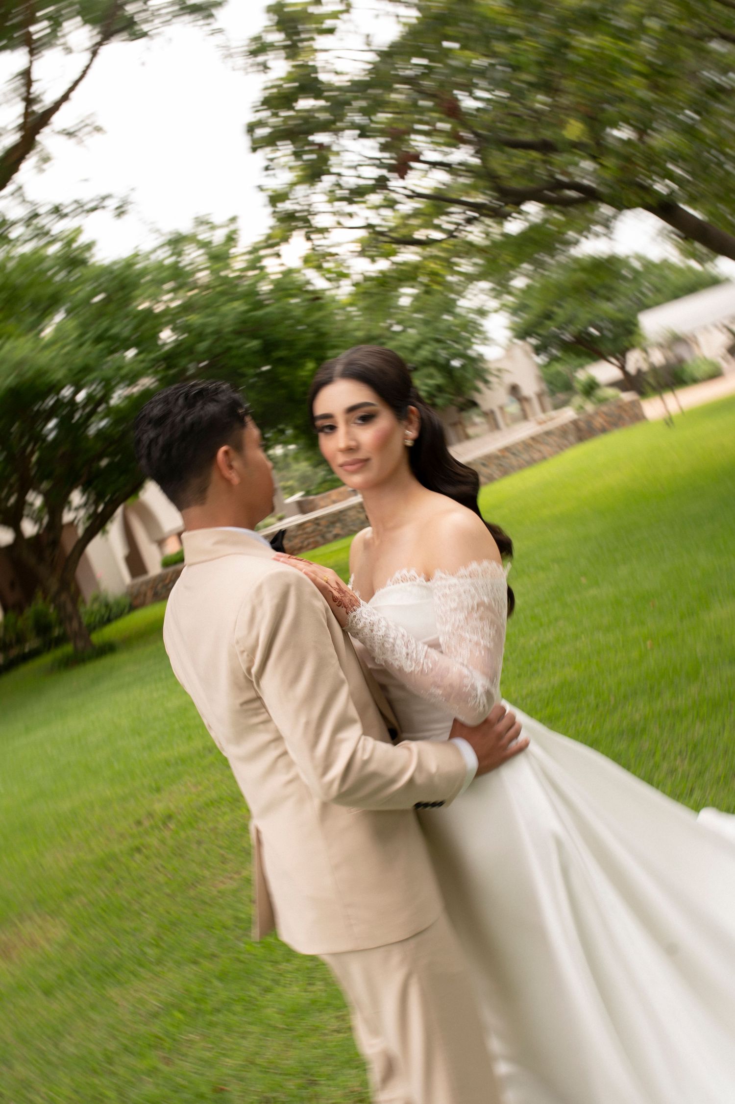 Romantic wedding couple embrace in garden setting with bride wearing off-shoulder gown.