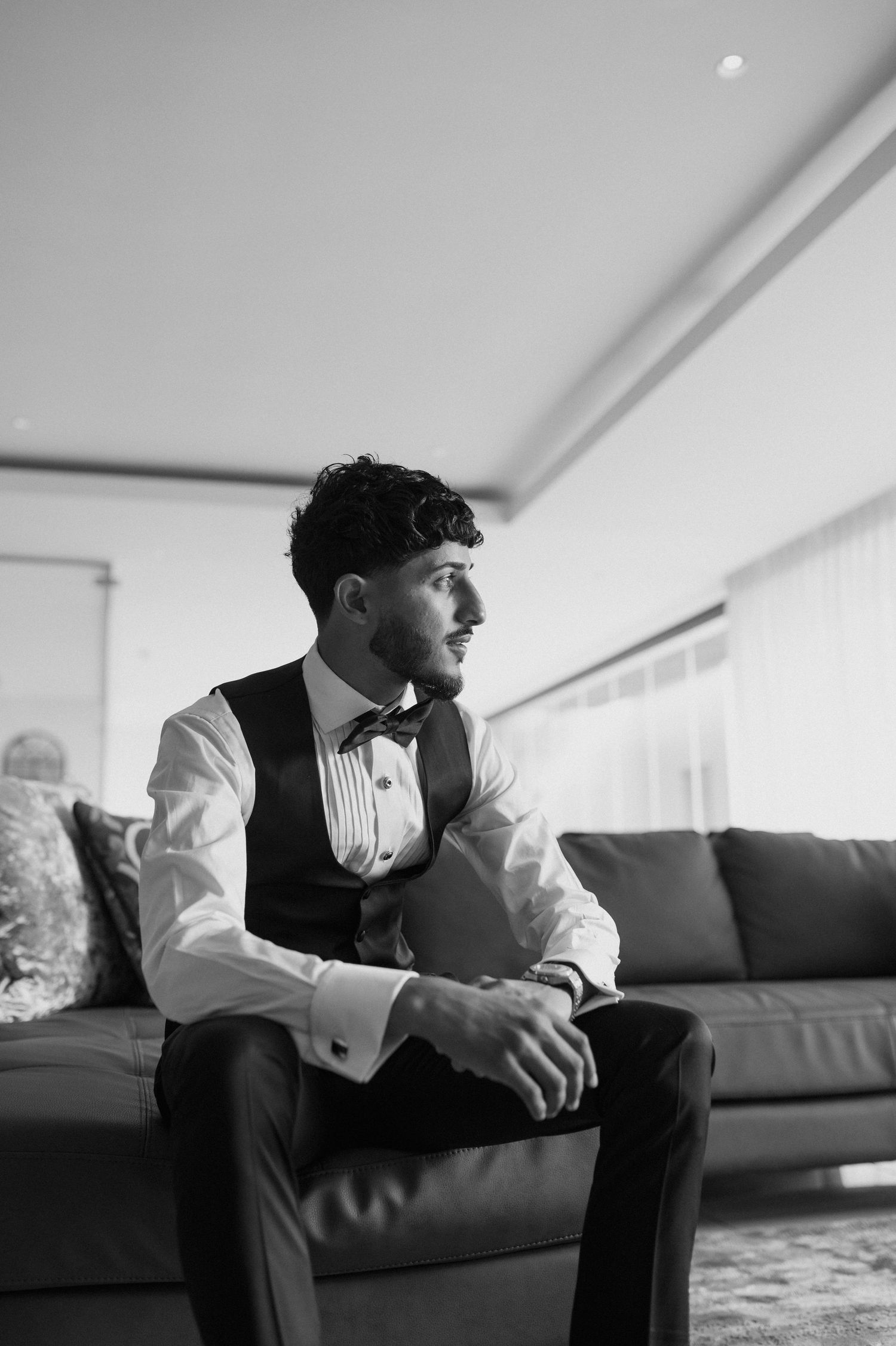 A formal portrait in black and white of someone in wedding attire sitting thoughtfully on a couch.