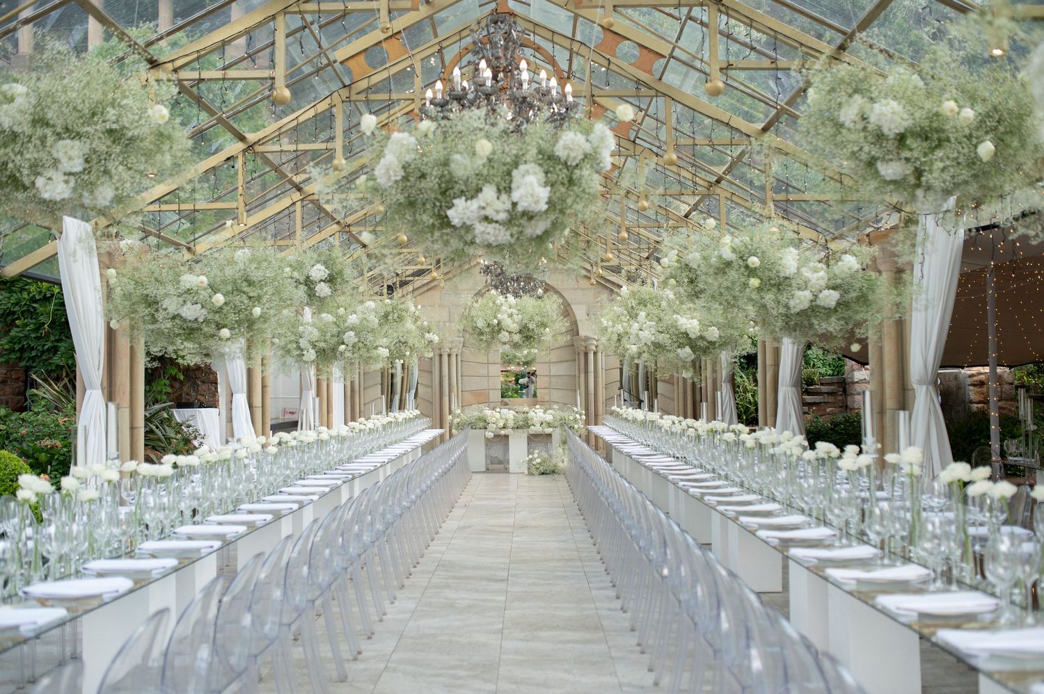 Elegant greenhouse wedding reception setup with crystal chandeliers and white floral arrangements.