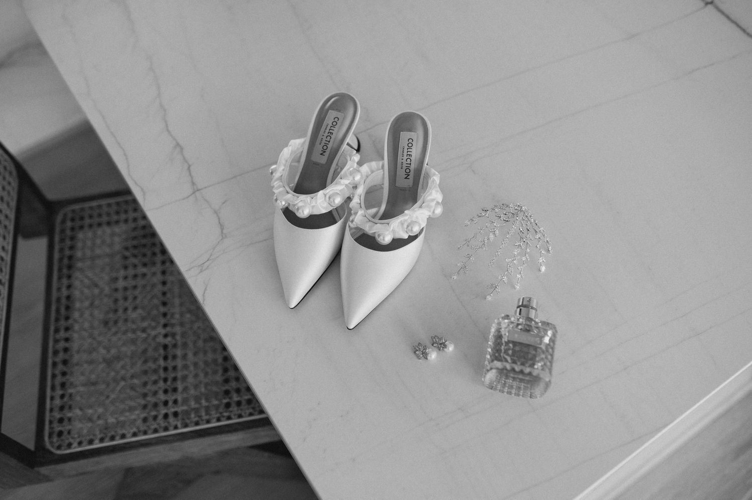 Elegant white bridal shoes and perfume bottle arranged on a marble surface in black and white.