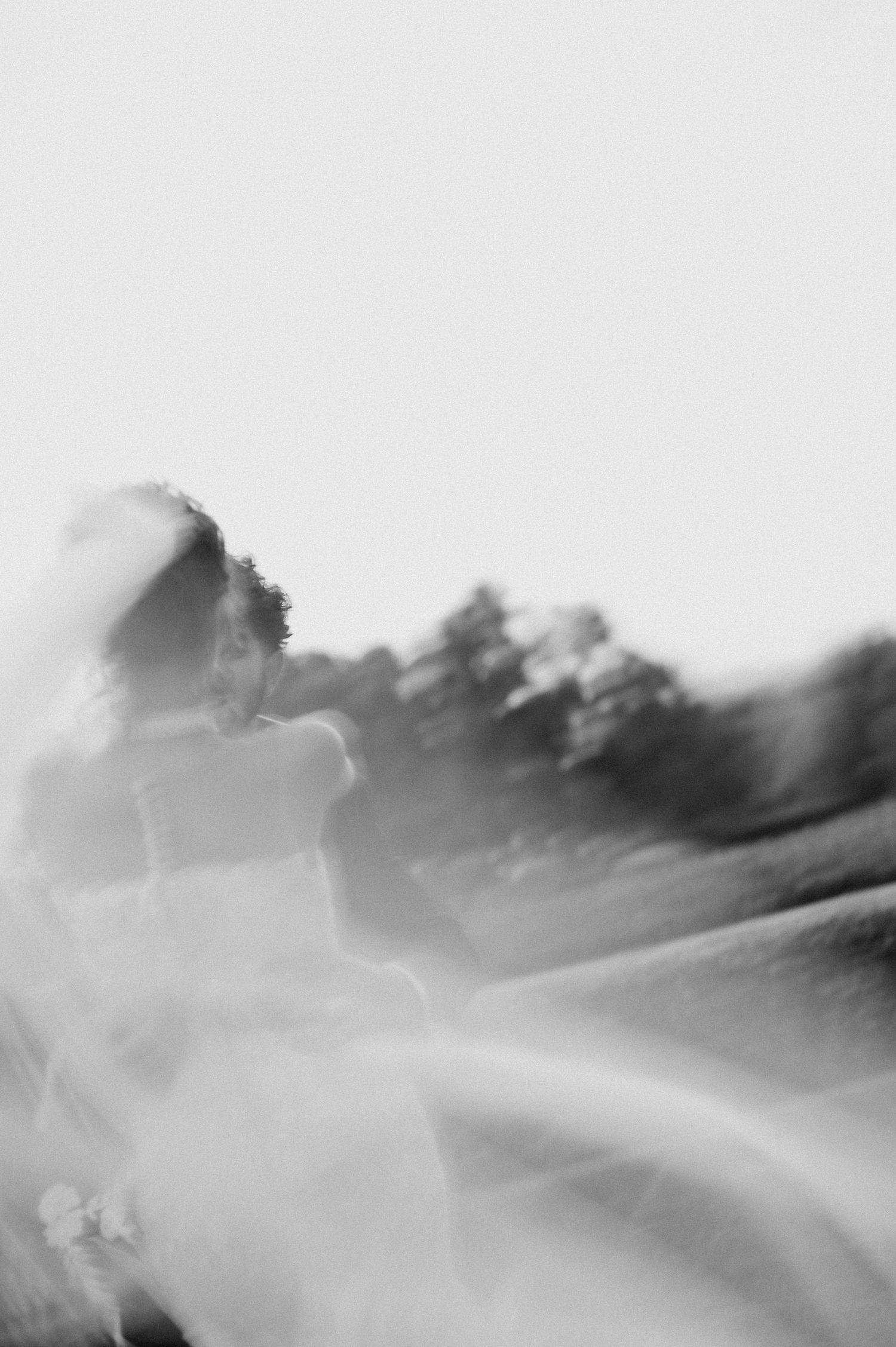 Artistic motion blur shot of flowing white wedding dress against light background.