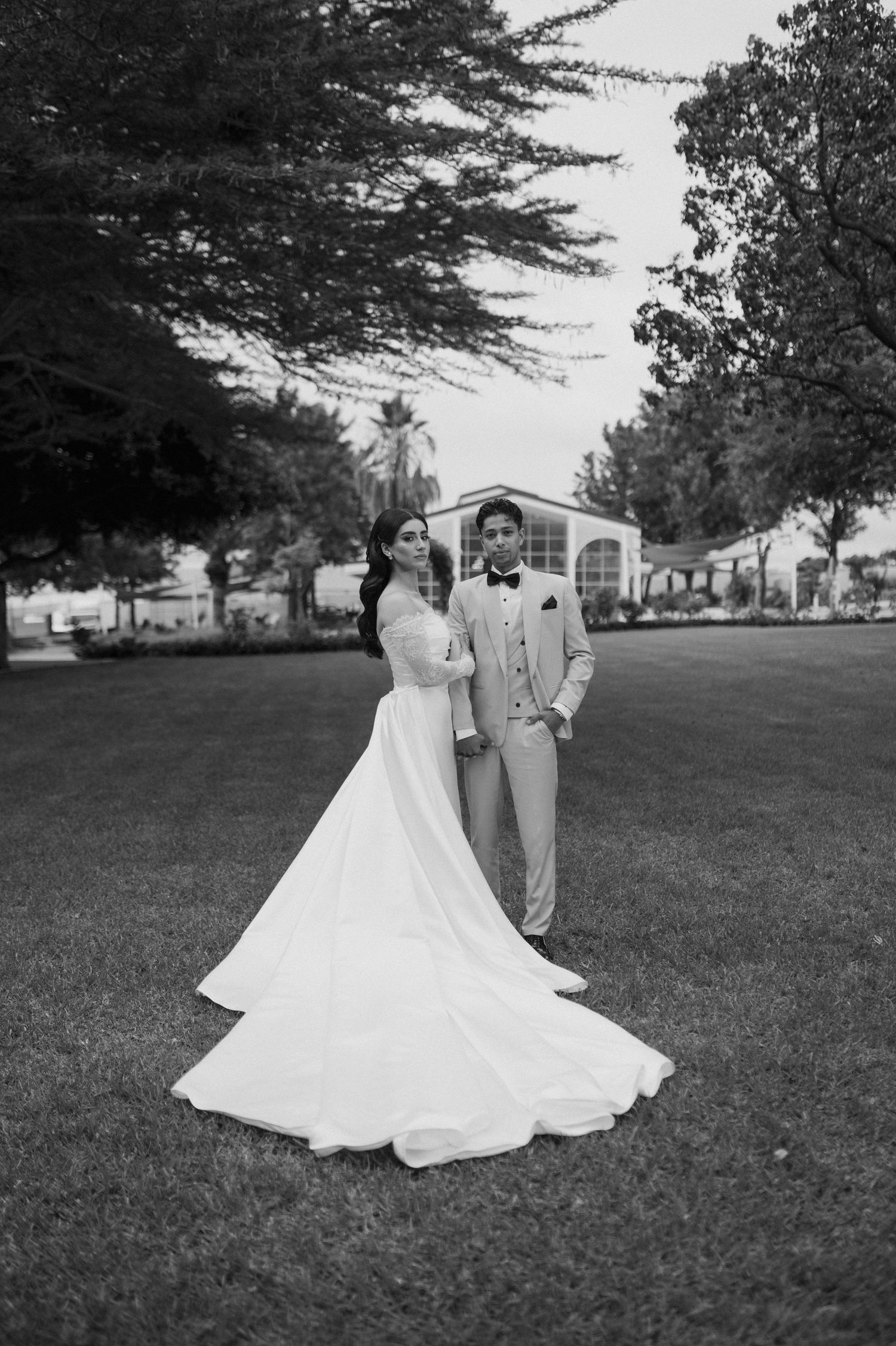 Black and white photo of couple on manicured lawn with dramatic flowing wedding gown train.