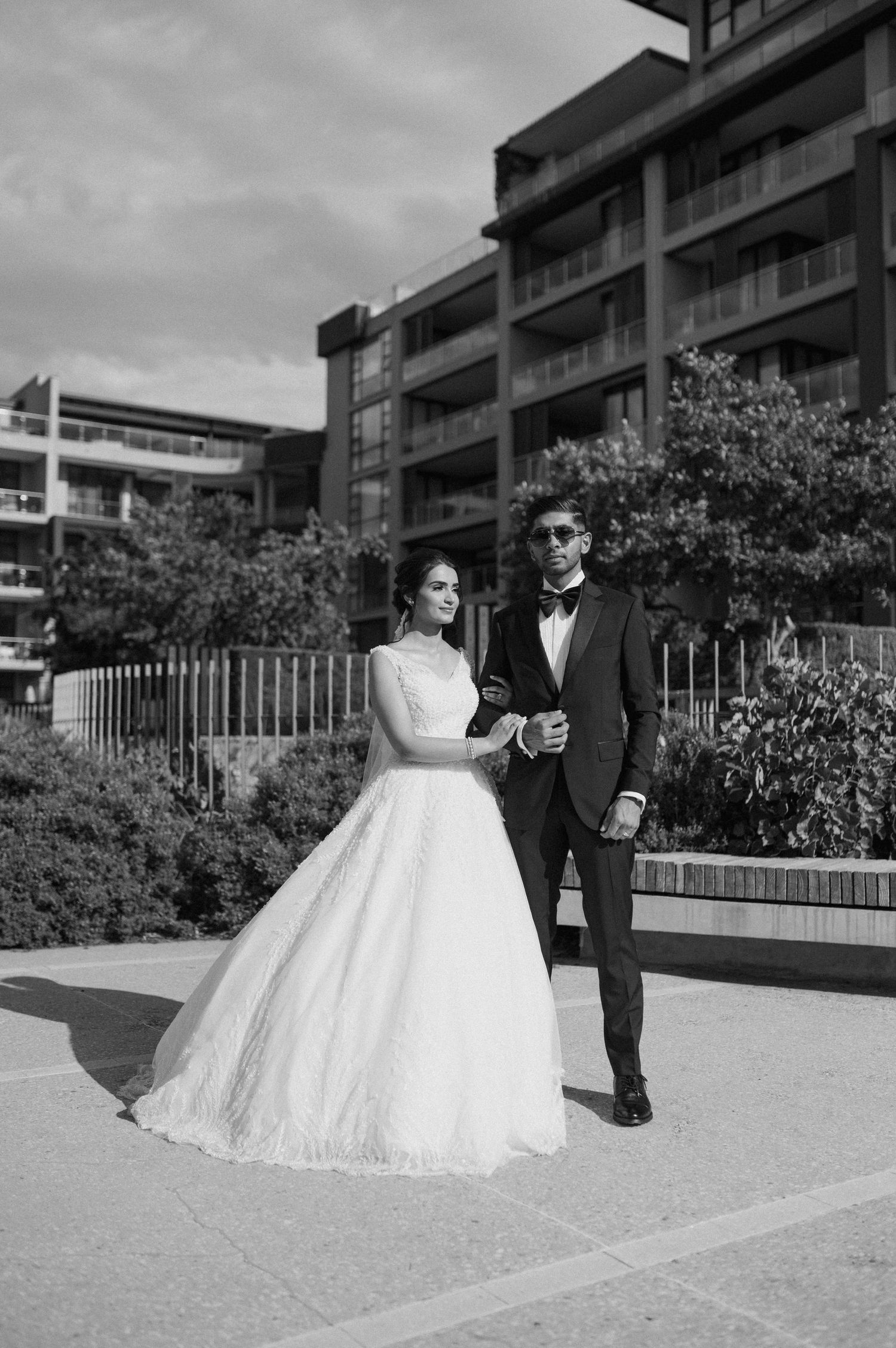 Black and white portrait of bride and groom standing outside modern apartment building.