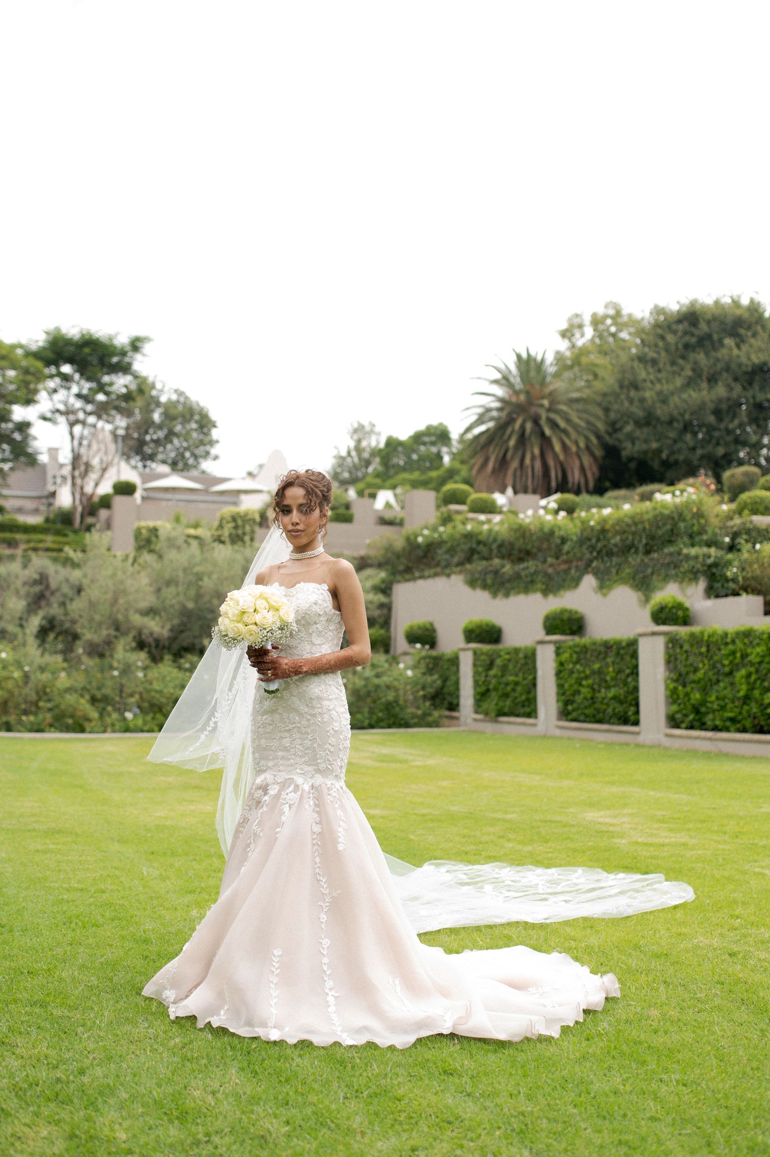 Beautiful white mermaid wedding dress with long train photographed in an elegant garden setting with palm trees.