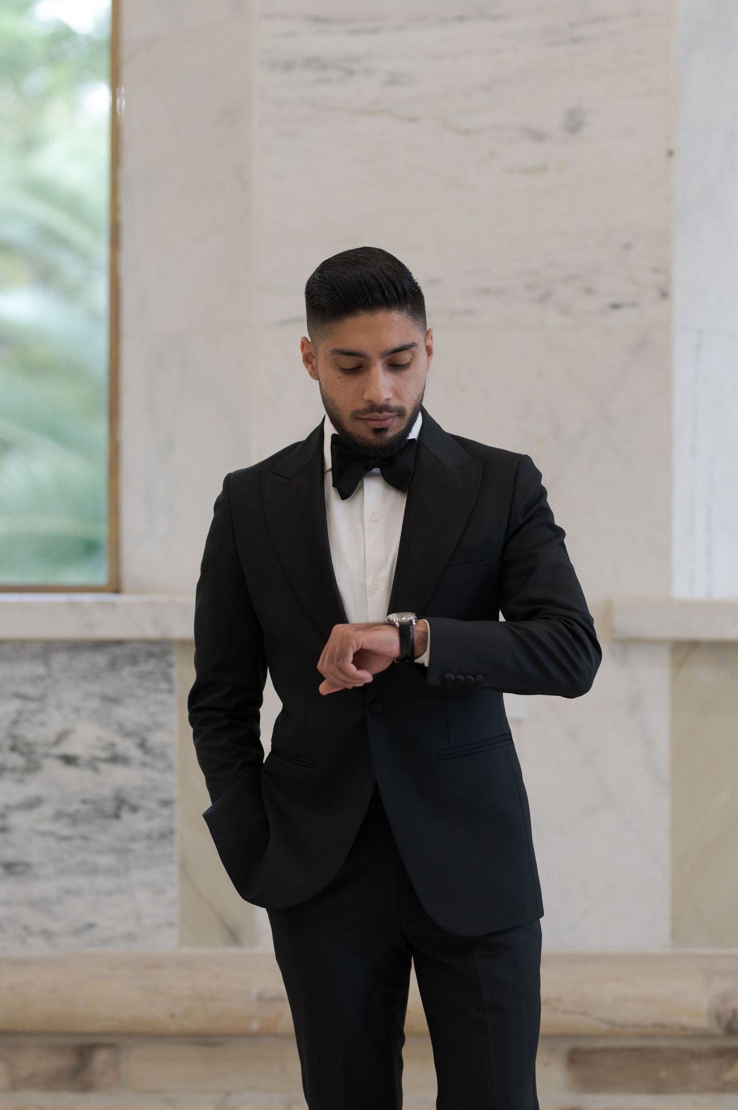 Groom in formal black tuxedo checking his watch before the ceremony.