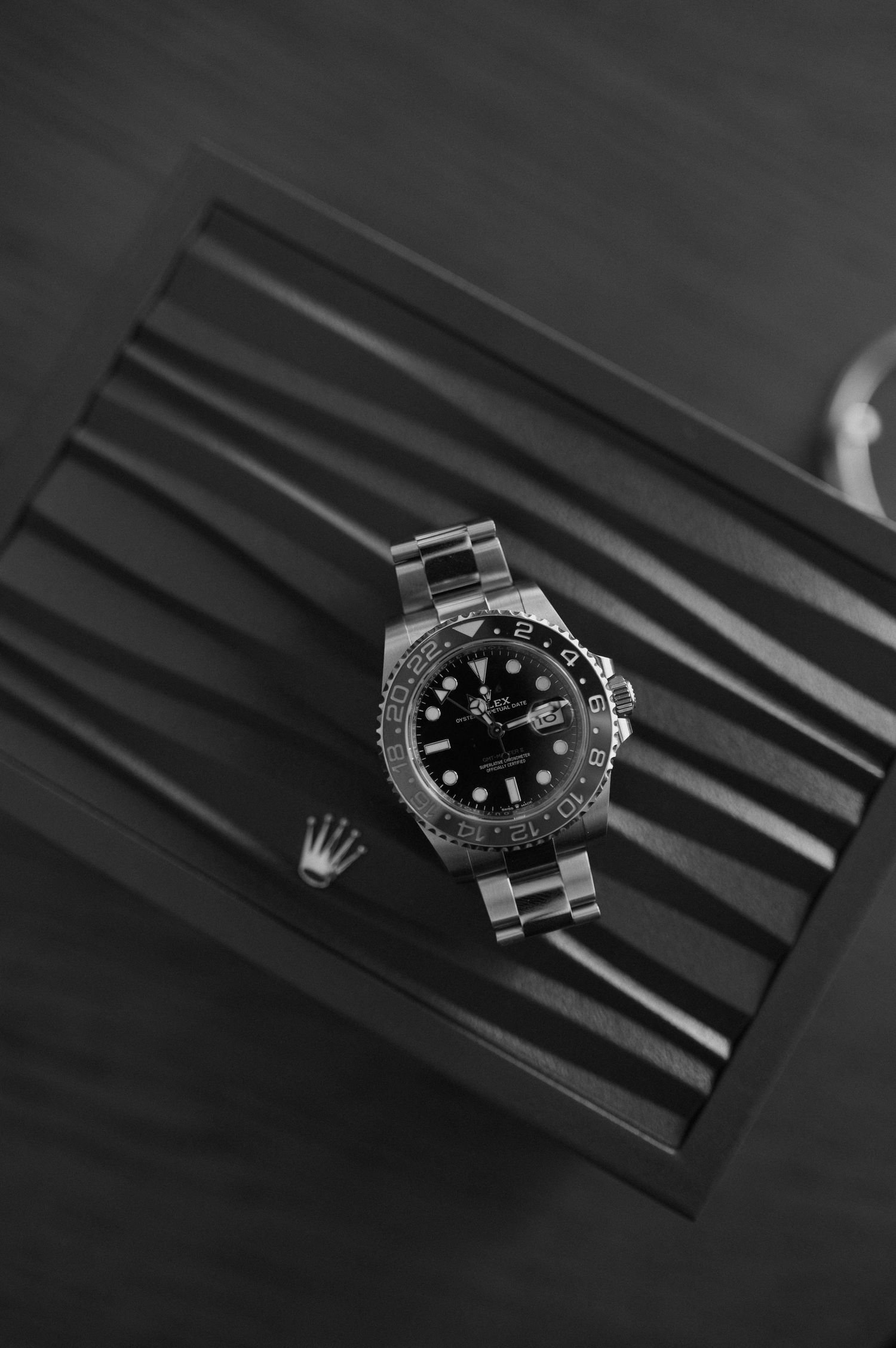 Black and white photo of a Rolex GMT-Master II watch resting on a striped Rolex watch box.