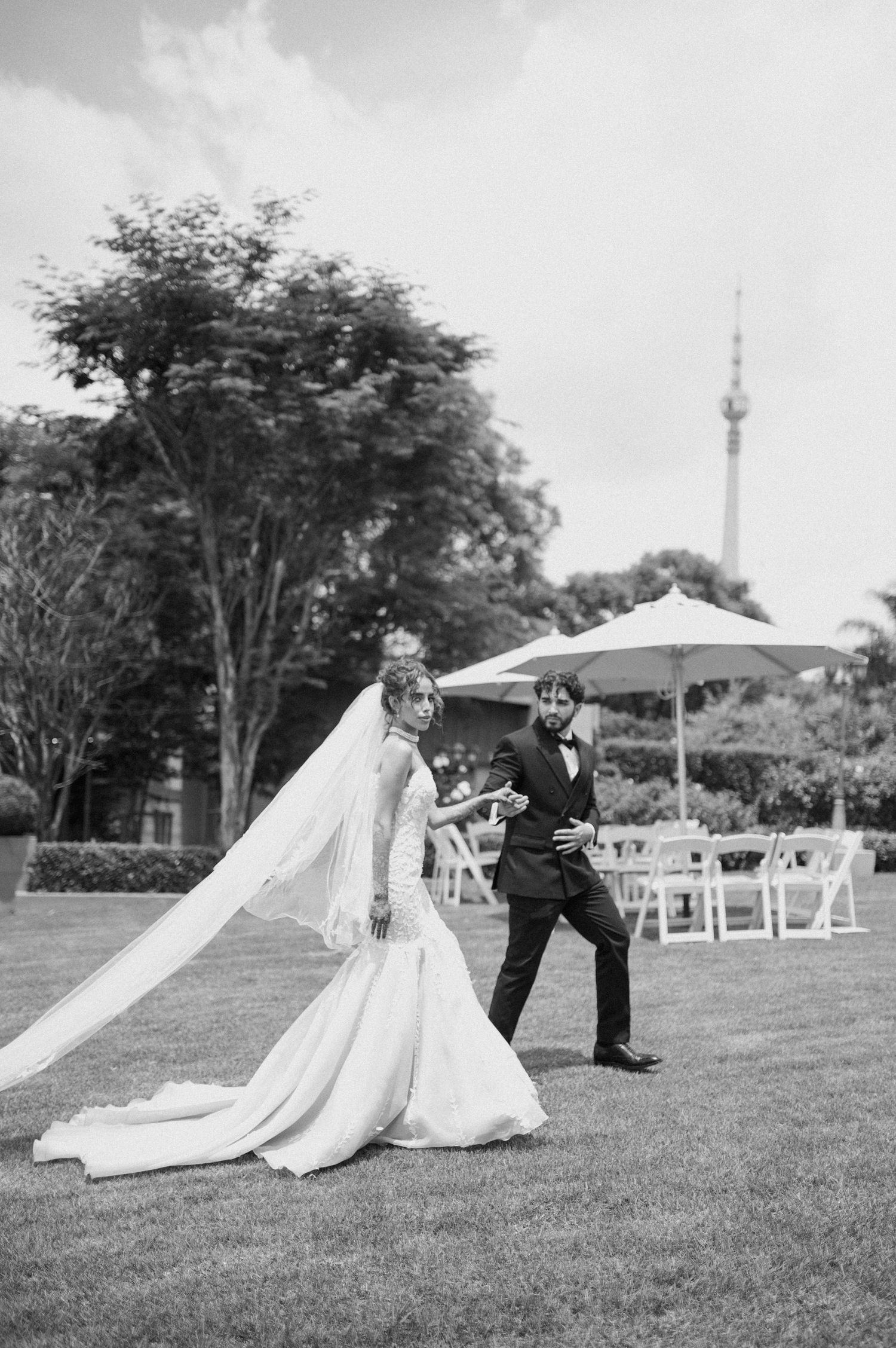 Black and white photo of a couple dancing joyfully on their wedding day with a flowing veil.