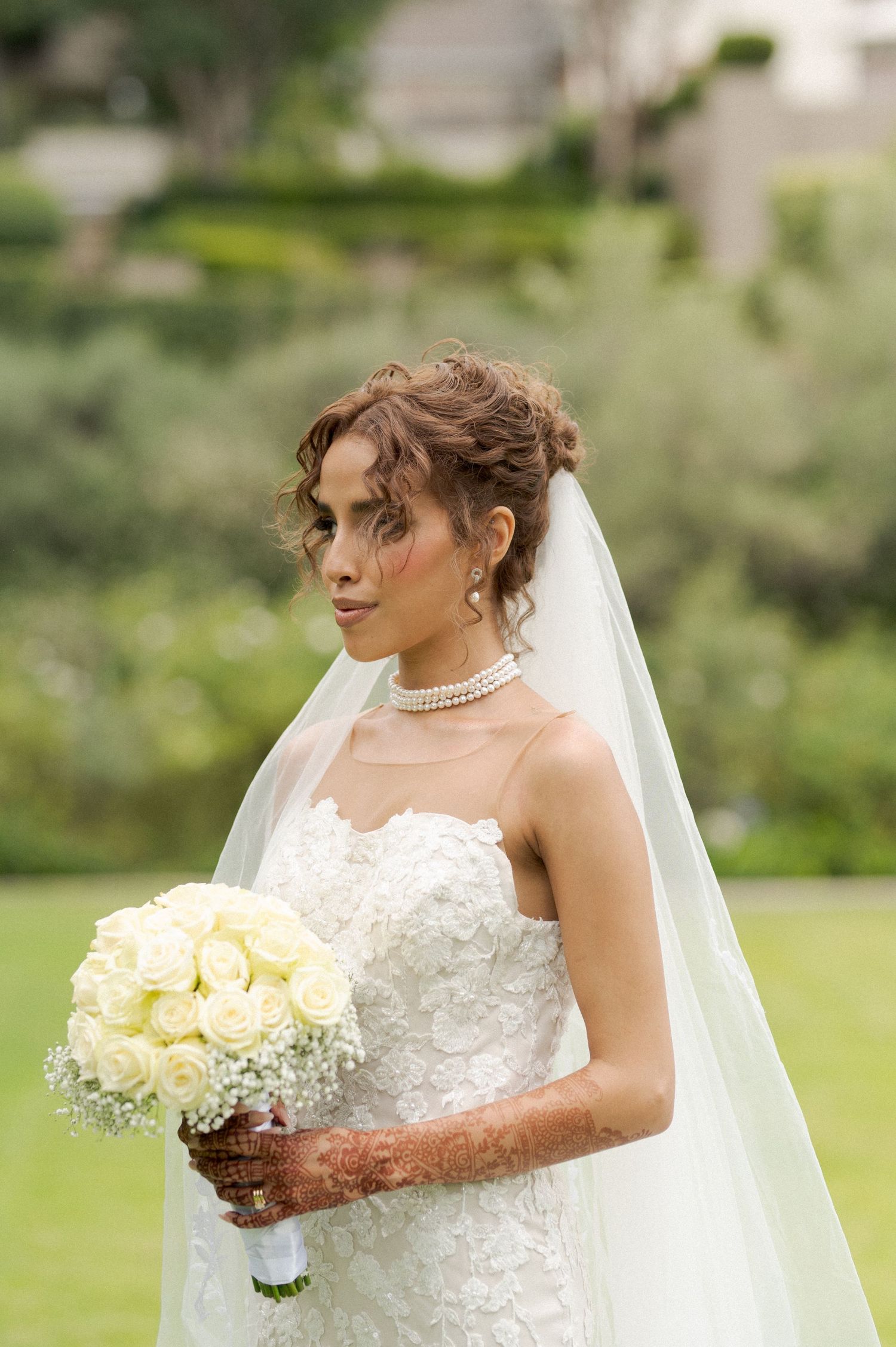 Bride in lace dress holds white bouquet while posing in garden setting.