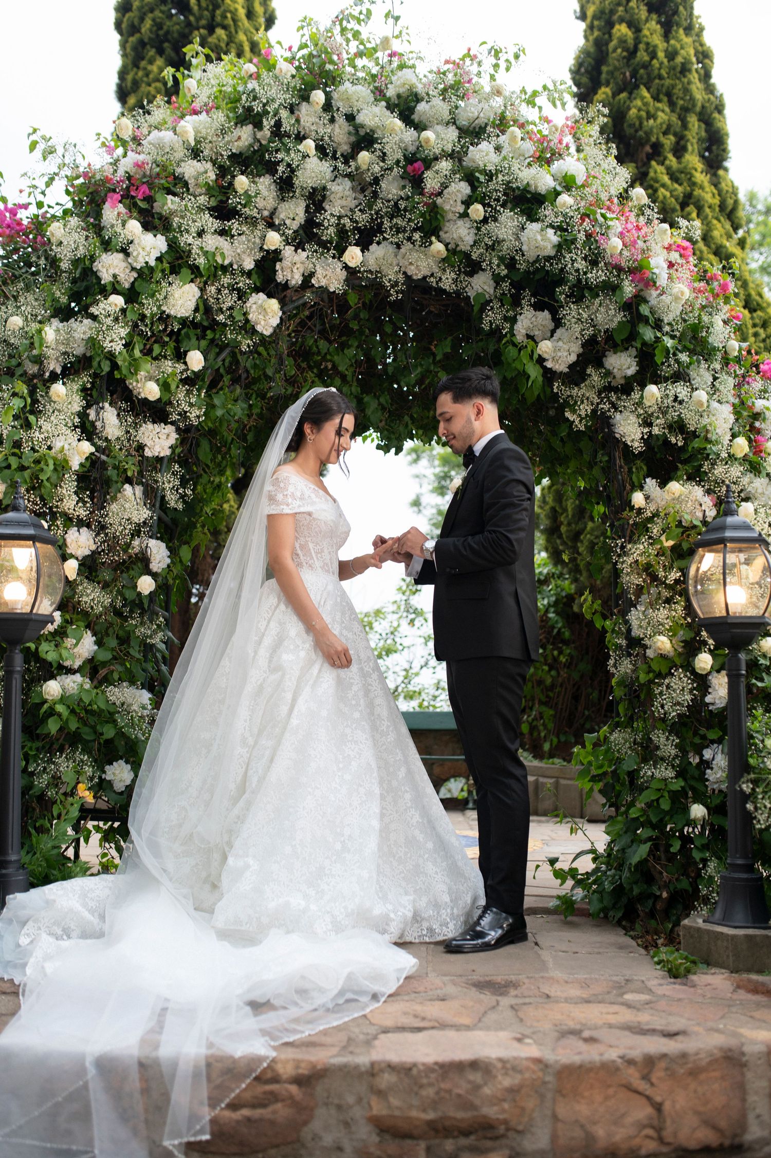A wedding ceremony moment under an ornate floral arch with hanging lanterns.