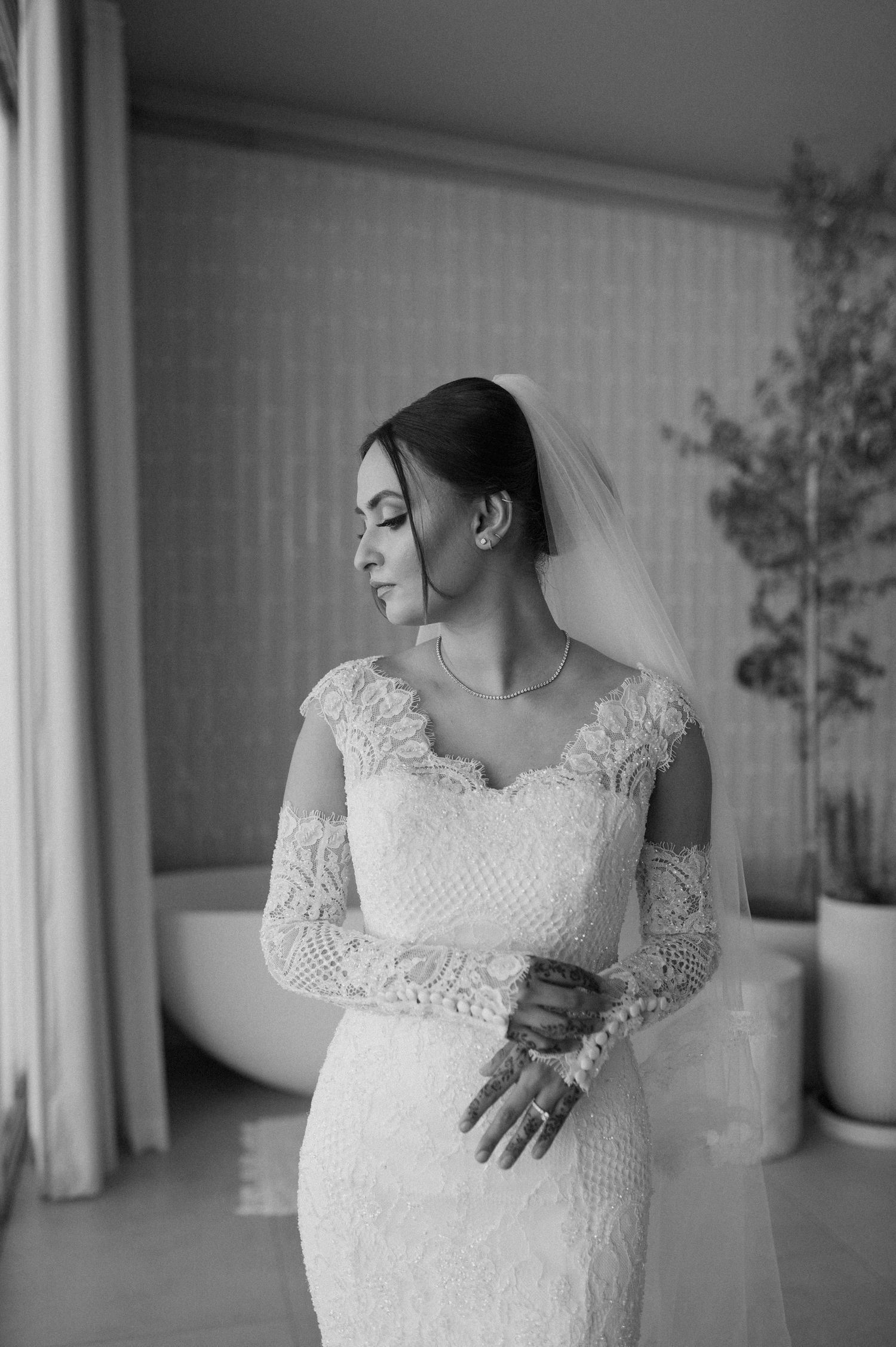 Elegant lace wedding dress with long sleeves and delicate veil shown in black and white profile view.