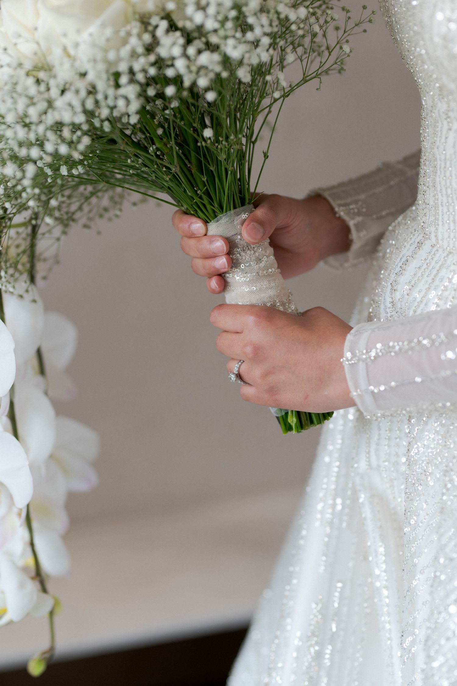 Close-up of hands holding delicate baby's breath and white floral bouquet wrapped in lace.