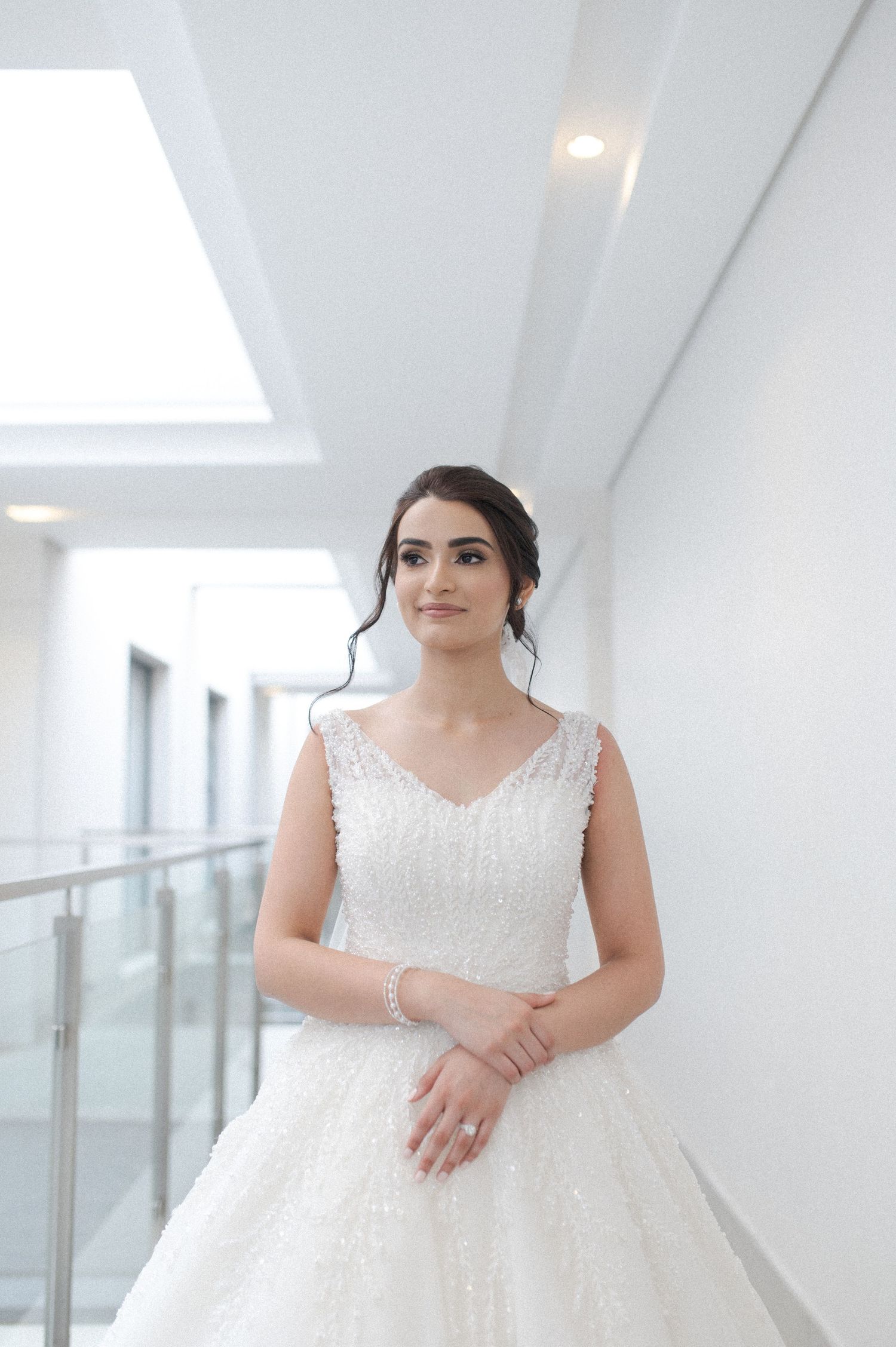 Bride wearing elegant white ball gown with lace details in bright modern hallway.