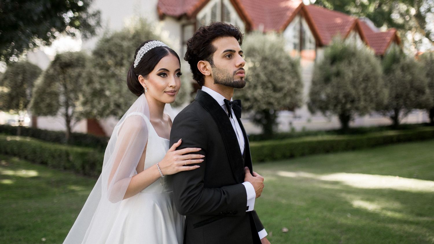 Bride and groom pose elegantly in front of Tudor-style buildings during wedding shoot.