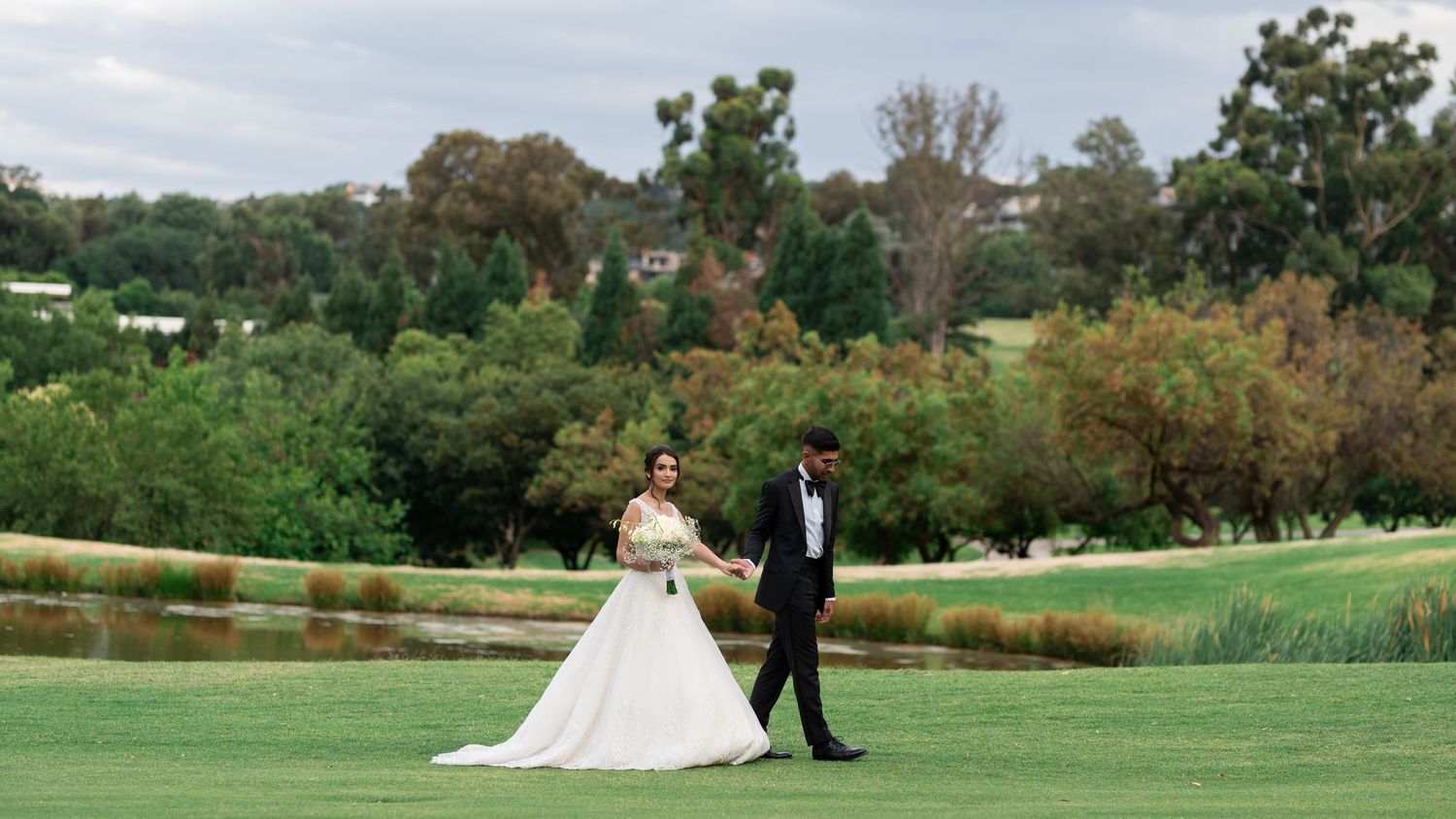 A bride and groom walk hand in hand across a lush green golf course.