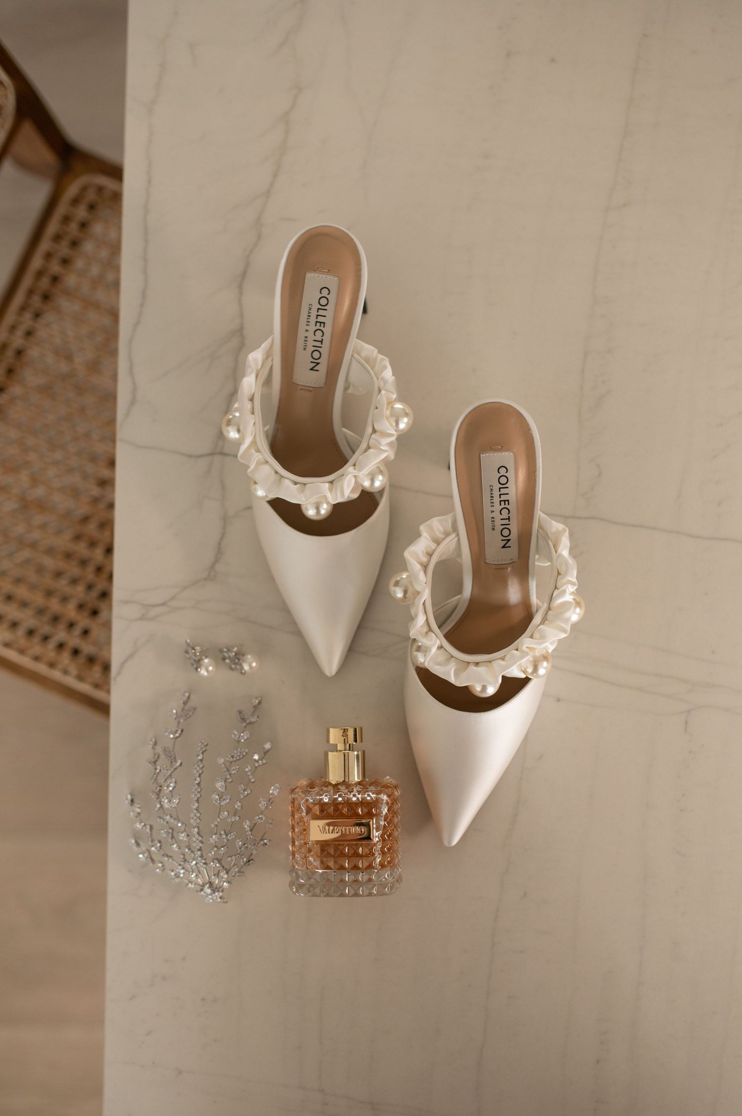 White designer mules with pearl trim displayed next to perfume and crystal accessories.