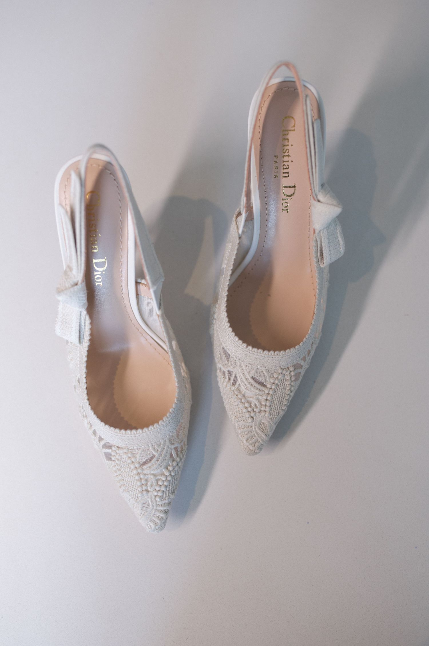 Elegant white lace wedding shoes with pointed toes and delicate bow details on a light background.