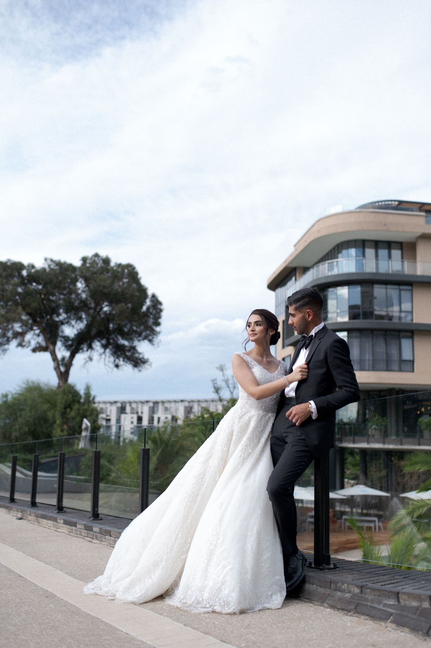 Newlyweds posing outside modern building with scenic backdrop.