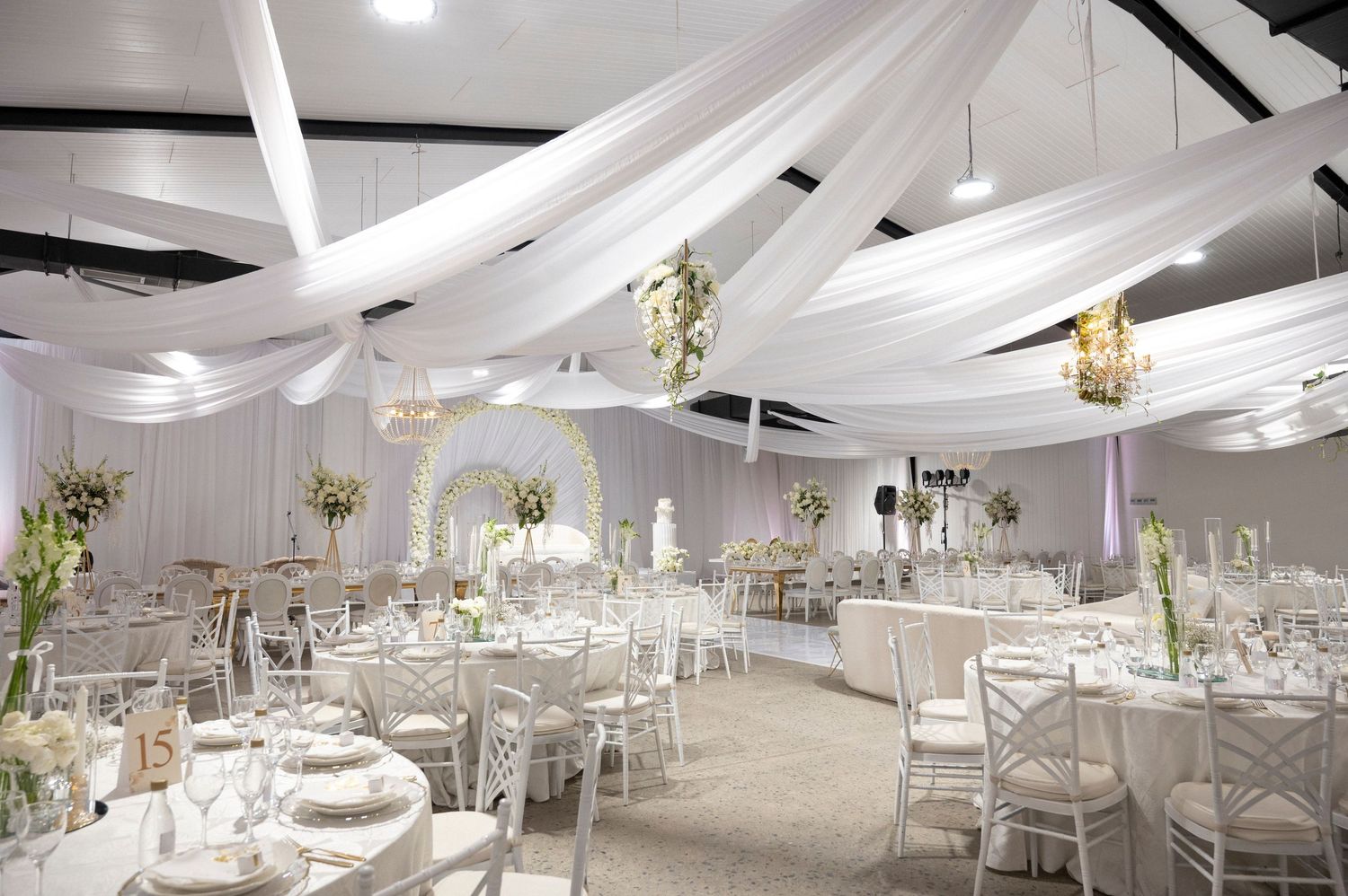 Modern wedding reception hall with white decor, crystal chandeliers and draped ceiling details.