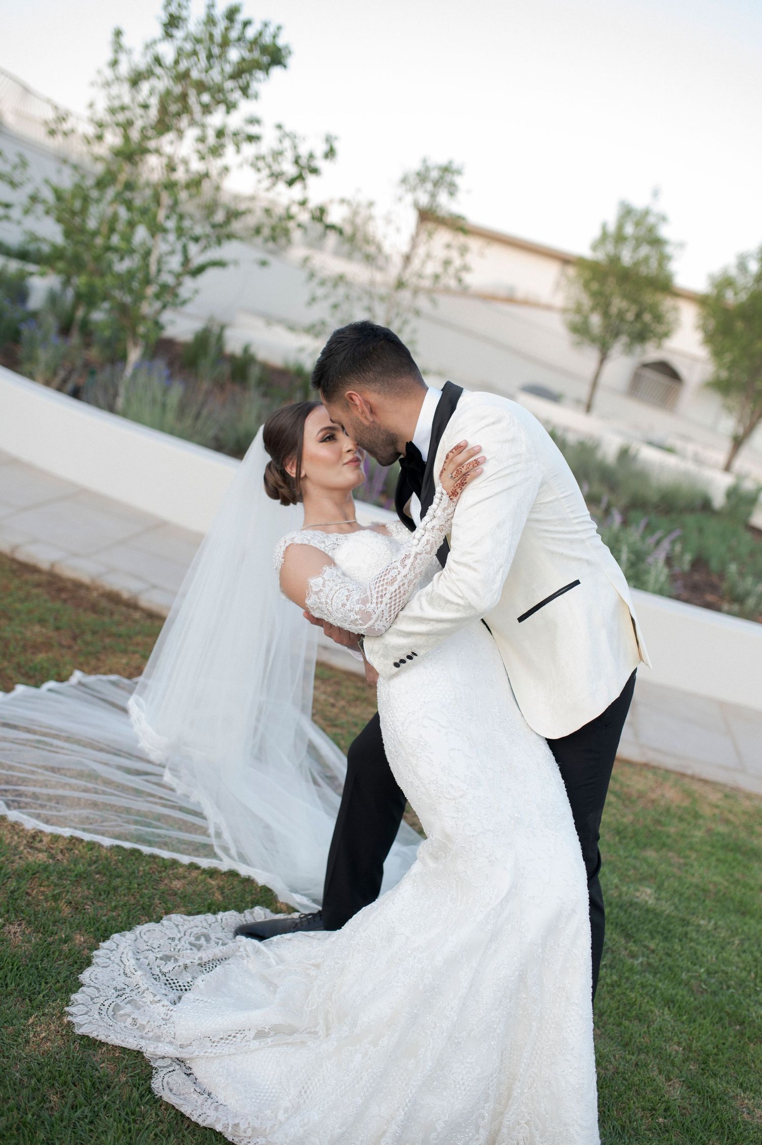 Romantic wedding portrait with flowing veil against landscaped garden backdrop.