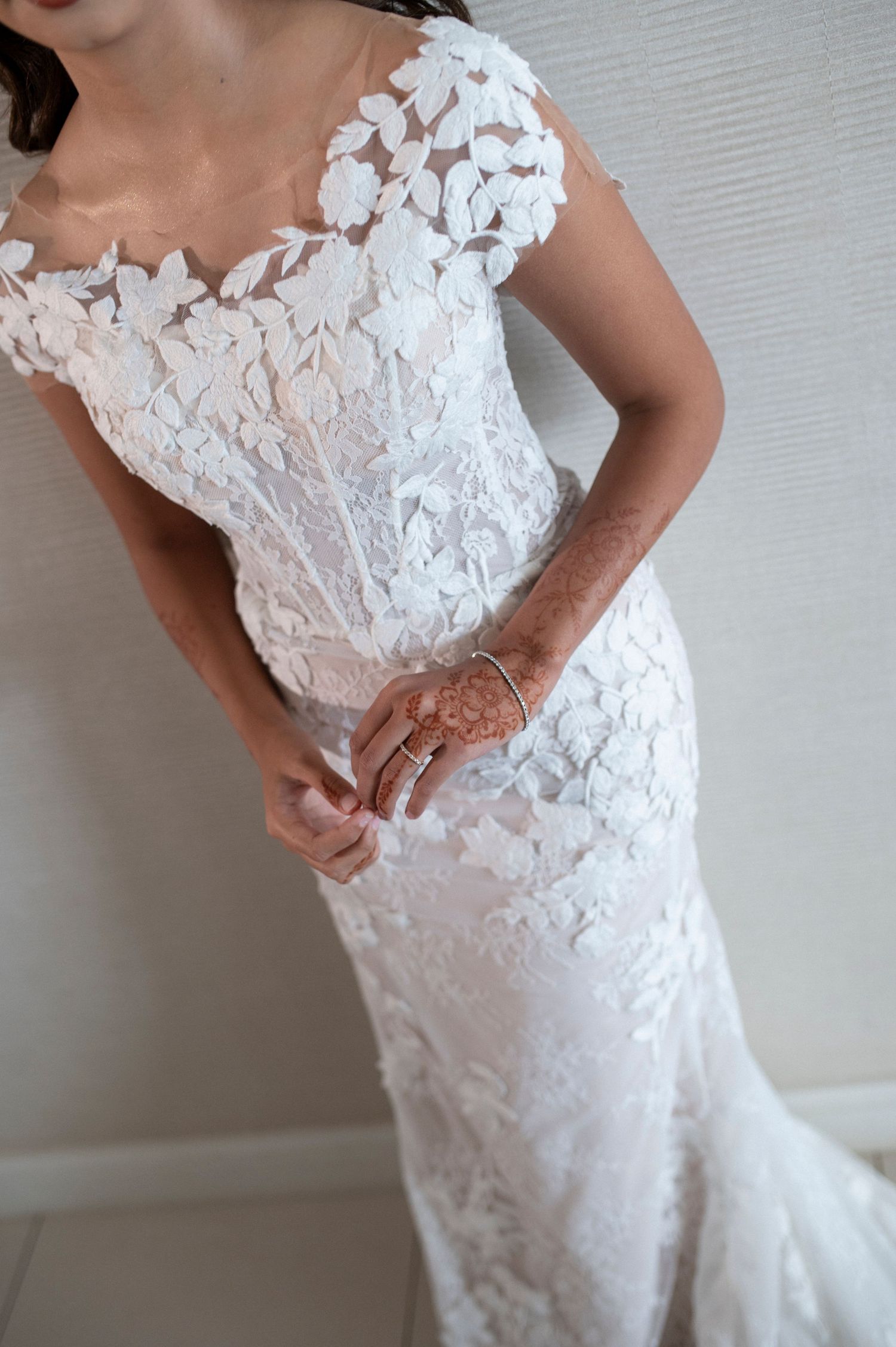 Close-up detail of intricate floral lace pattern on a fitted white wedding dress.