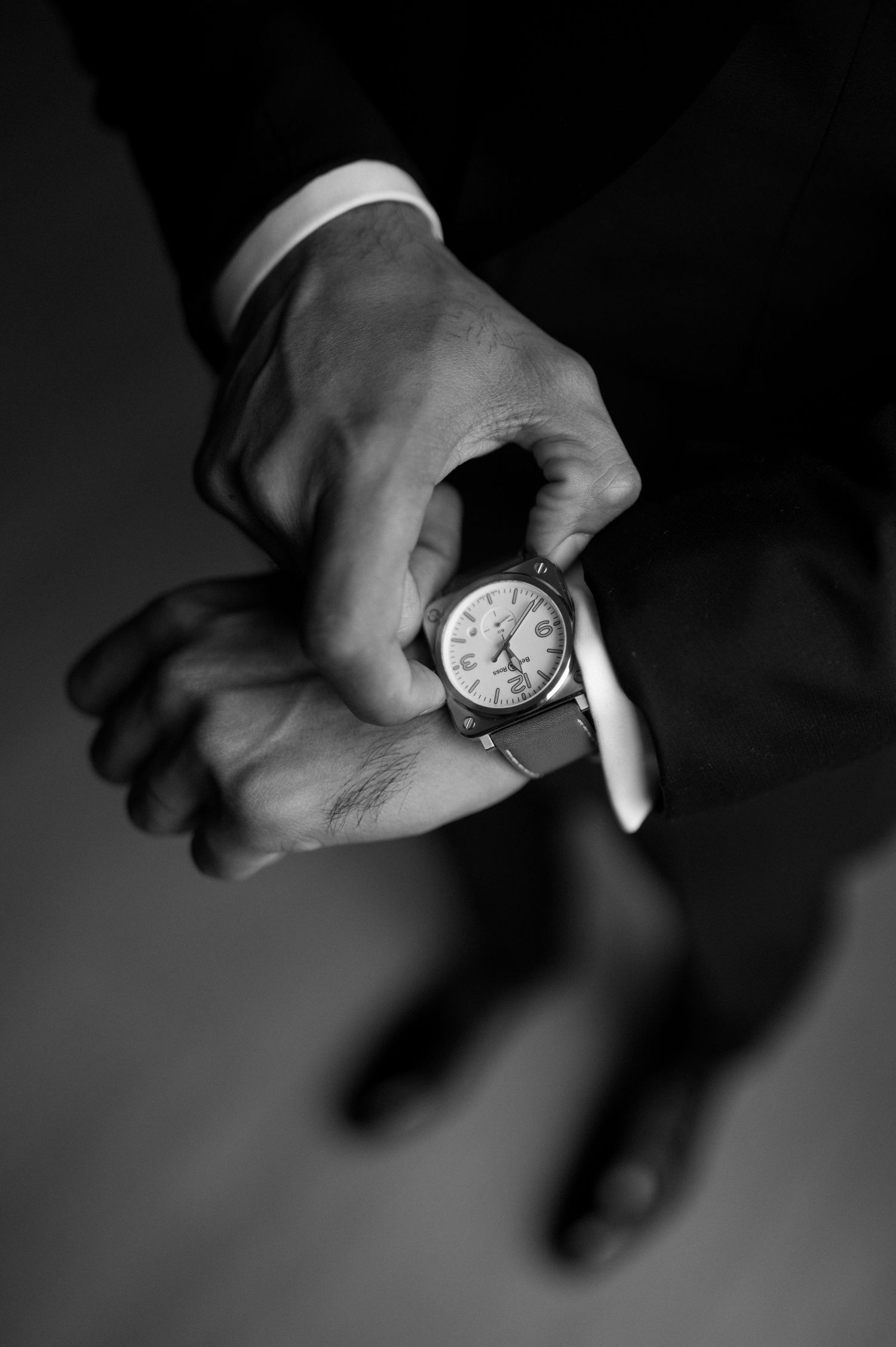 Close-up of hands checking time on classic wristwatch in black and white.