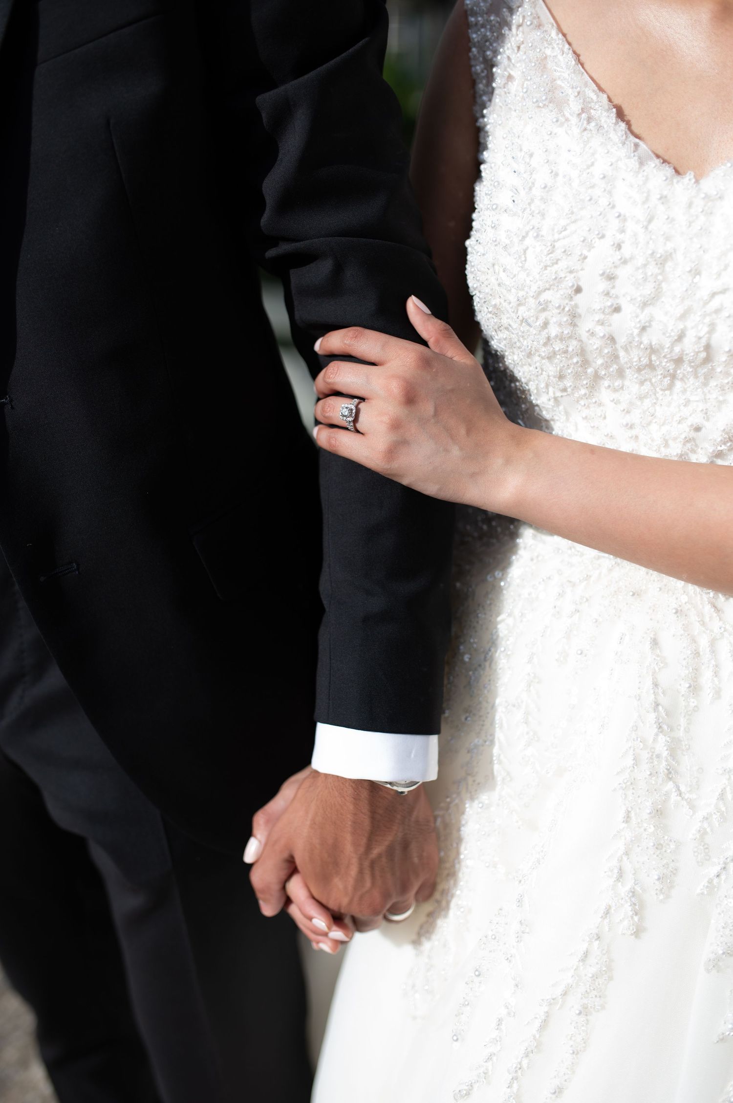 Close-up detail of bride's hand with wedding ring holding groom's arm.
